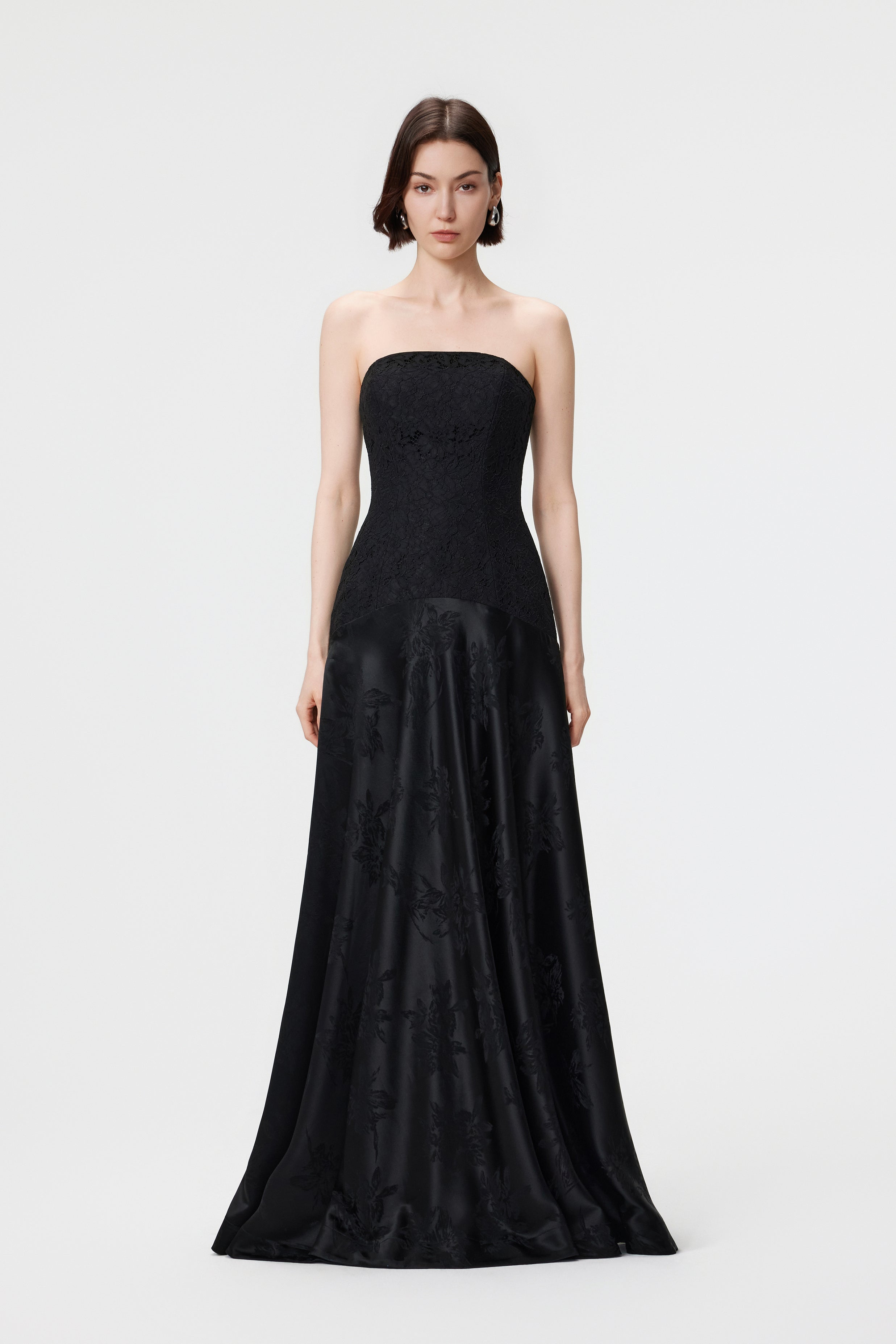Front view of the AENSO Vera gown in Black; a statuesque silhouette featuring a precision-paneled lace bodice, V-neckline, and a bias-cut floral jacquard skirt.