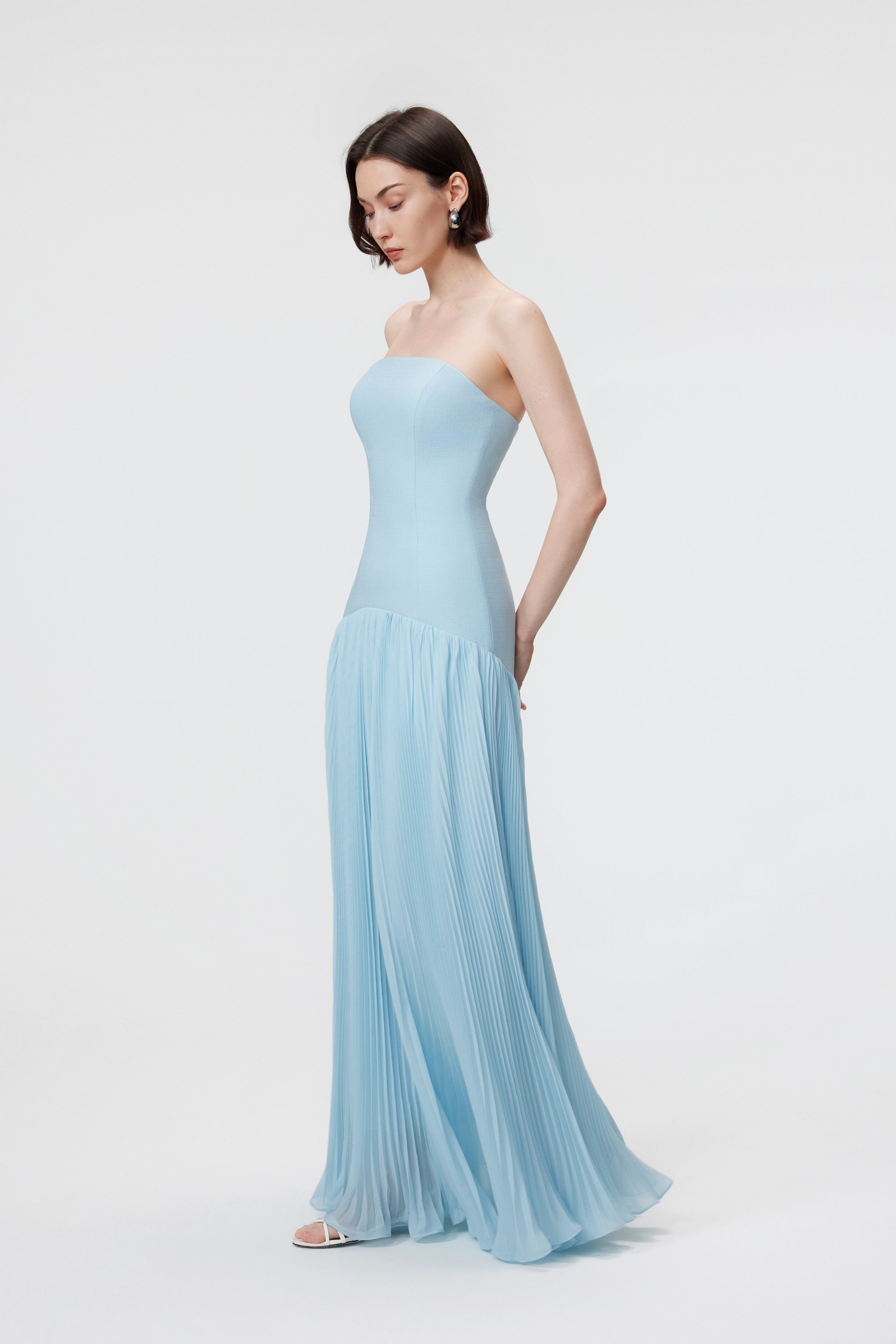 Luna Gown in Ether Blue, showcasing the structured bustier silhouette and the rhythmic flare of the floor-length sunray pleats in textured Naia™ acetate.