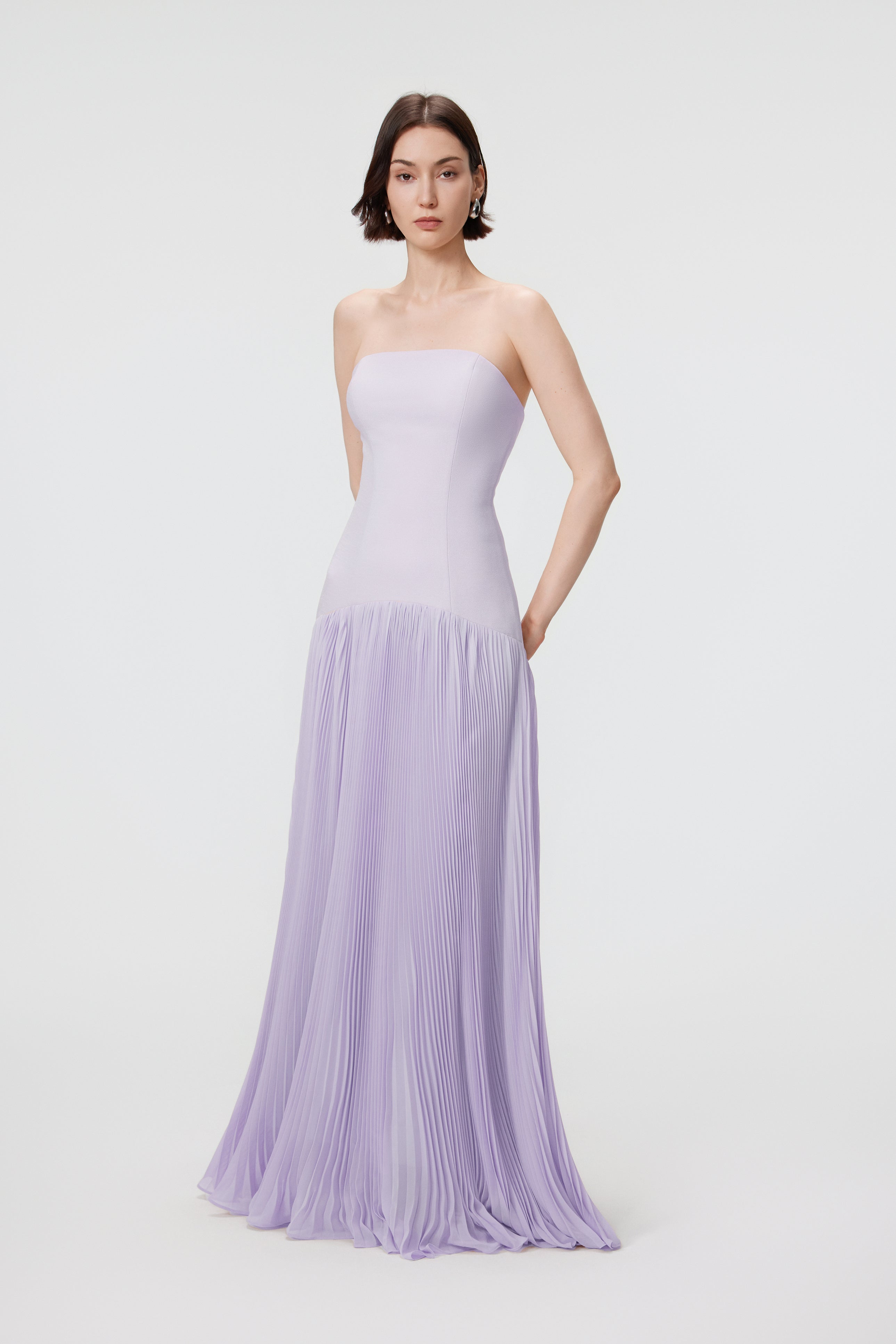 Side profile of the Luna gown in Cloudy Lilac, highlighting the fluid movement of the sunray pleats and the refined, architectural profile of the high-waisted bodice.