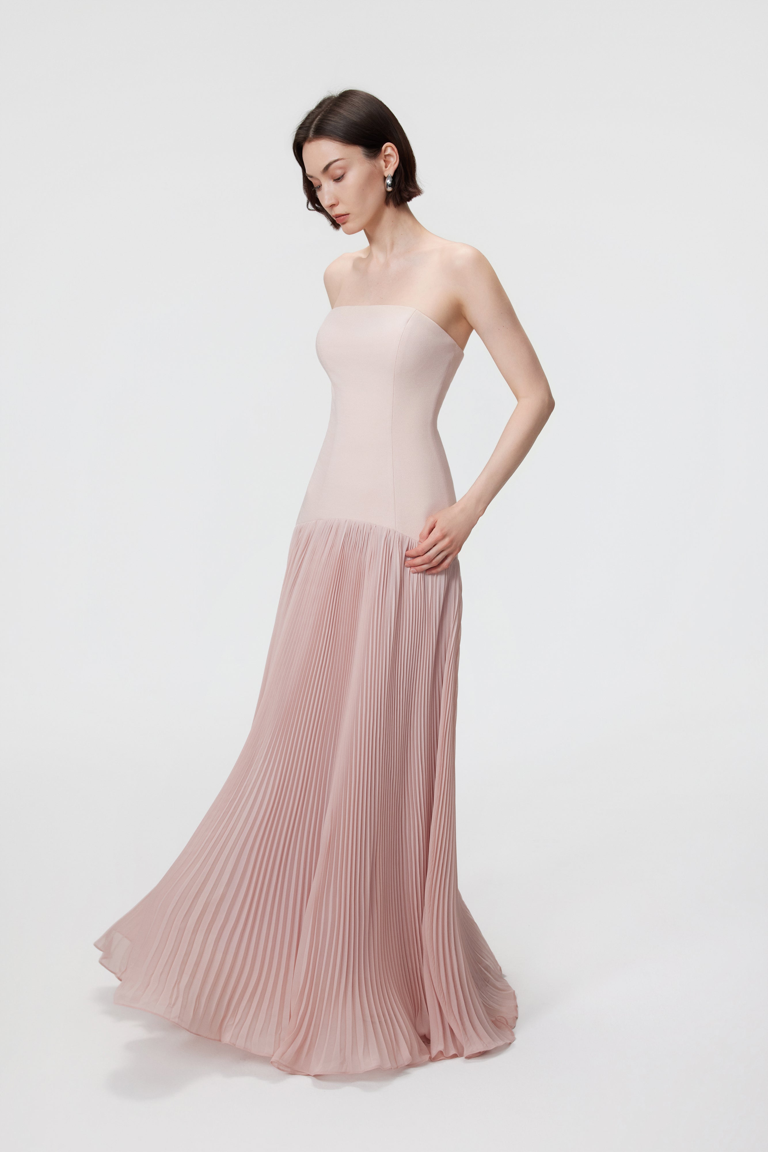 The voluminous sunray pleats on the Luna gown, demonstrating the interplay of light and shadow across the delicate rosewater hue.