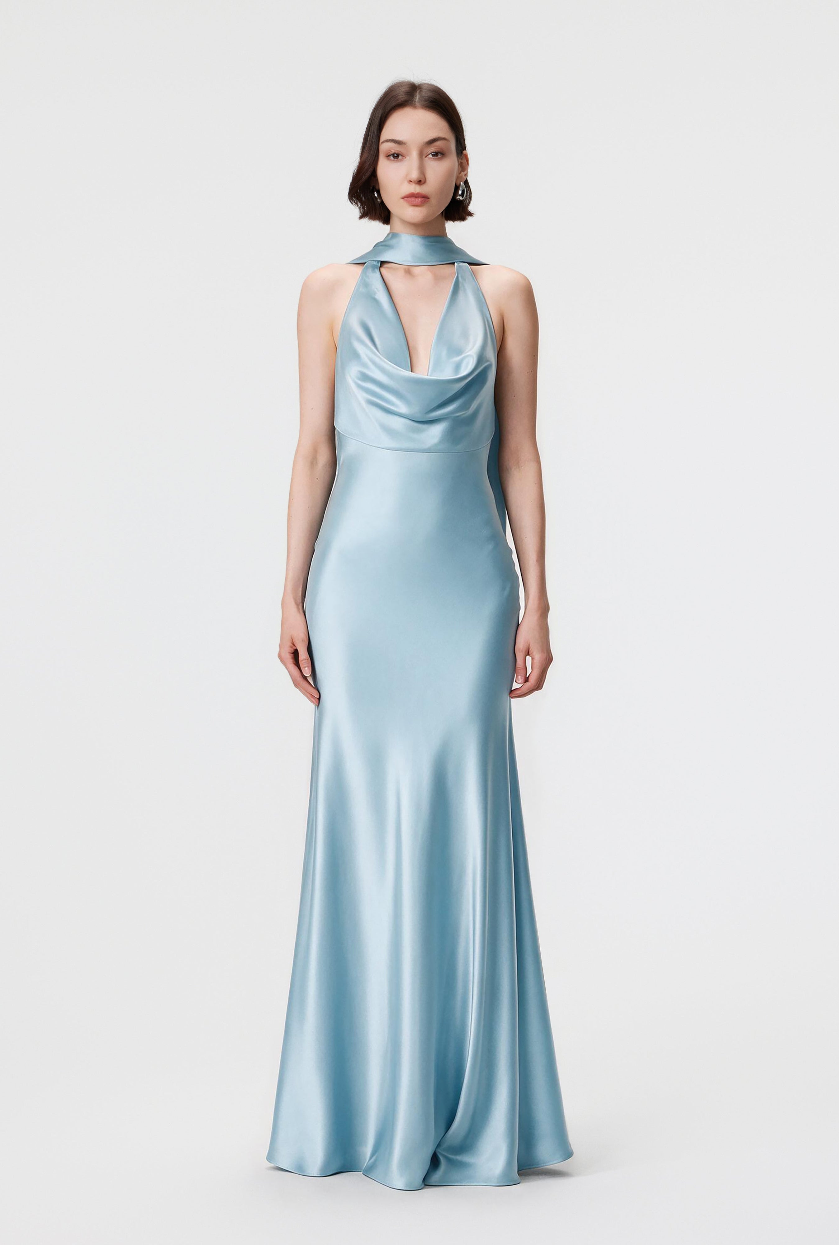 A model wears the Rhea dress in Ether Blue, featuring a draped cowl neckline and a floor-length, bias-cut silhouette in luminous Naia™ Acetate satin.