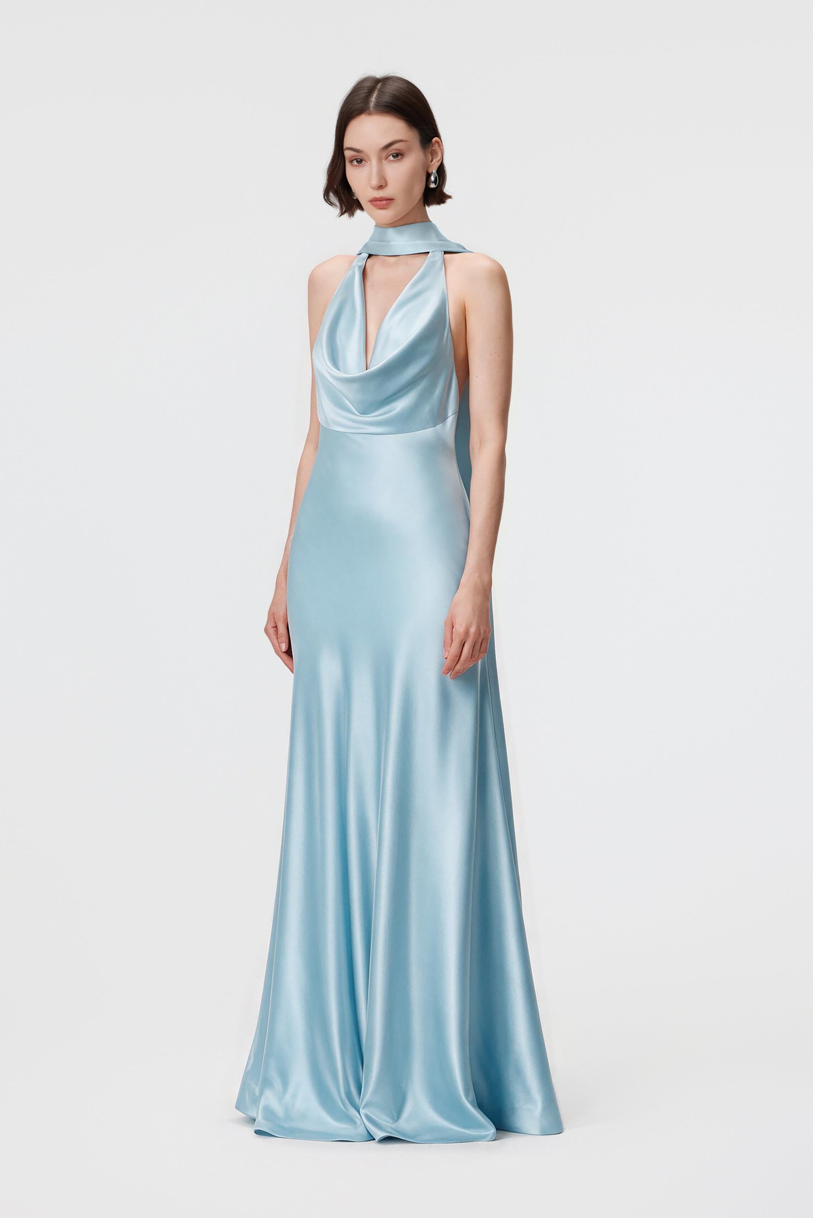 Model from the side wearing the Rhea dress in Ether Blue, highlighting the fluid cowl neckline, low open back, and floor-length, bias-cut silhouette in luminous Naia™ Acetate satin.