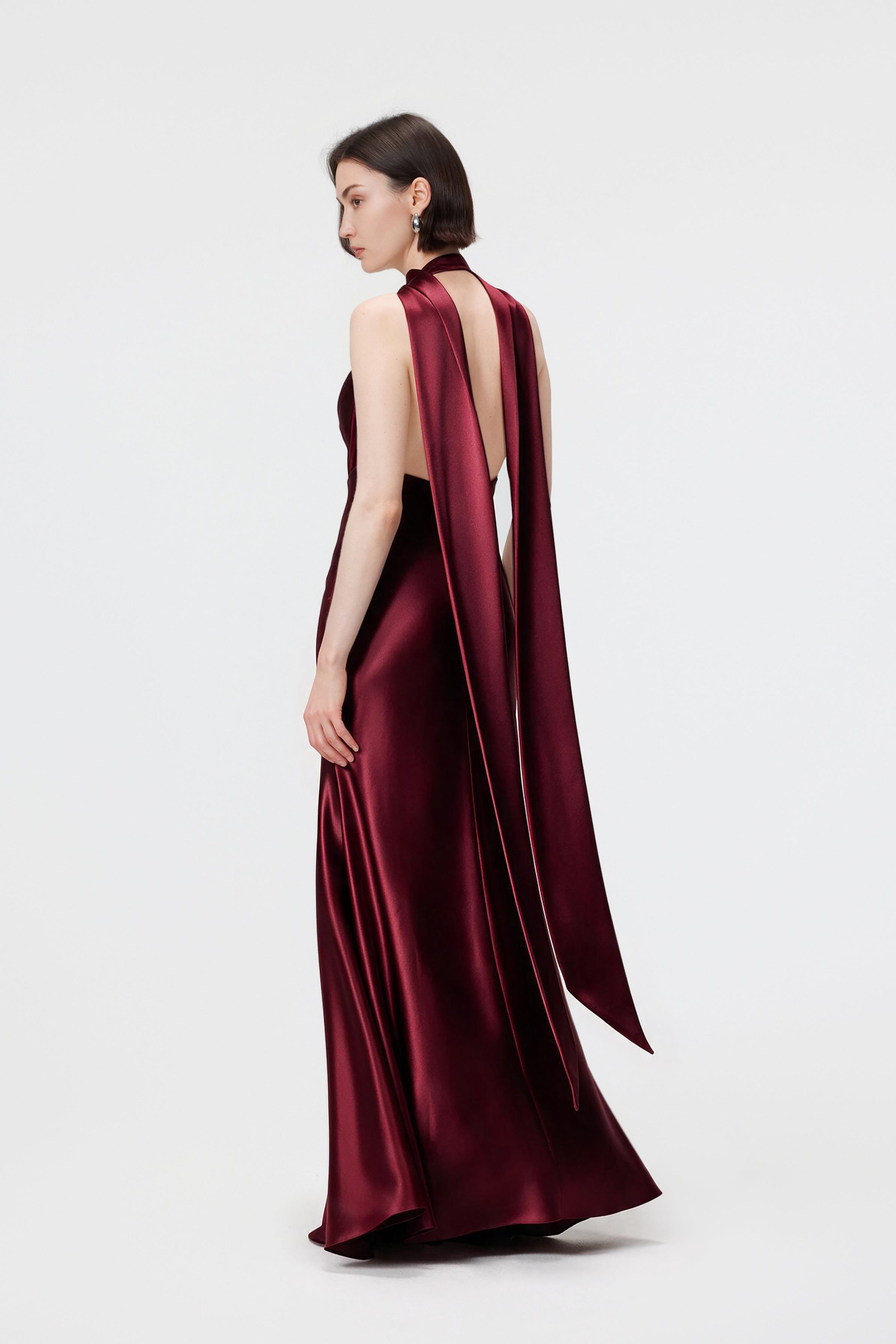 Model from the back wearing the Rhea dress in Red Berry, highlighting the fluid cowl neckline, low open back, and floor-length, bias-cut silhouette in luminous Naia™ Acetate satin.
