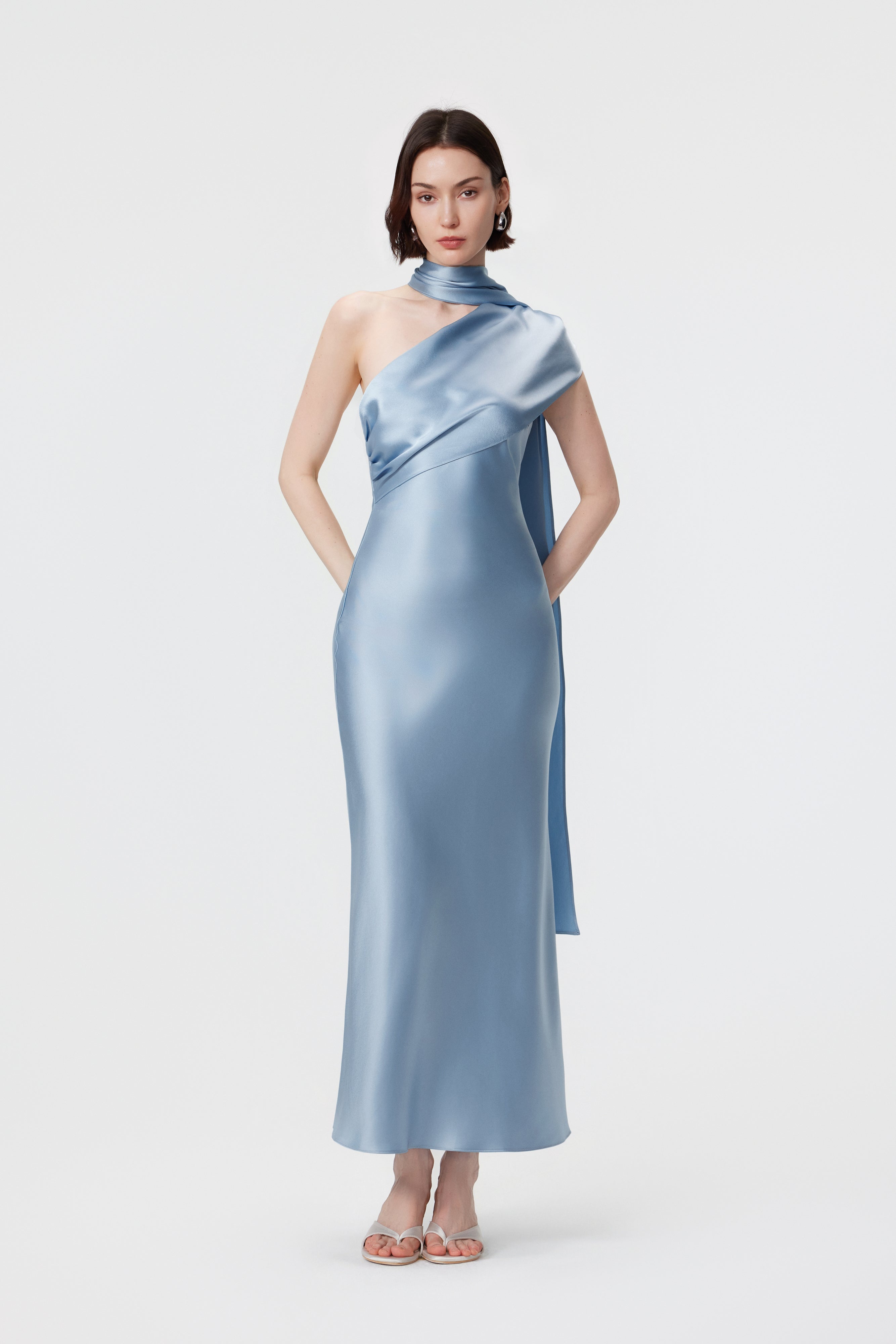 AENSO Lyra dress in Glacial Mist; front view featuring a sculptural high-neck wrap and one-shoulder drape in bias-cut satin.