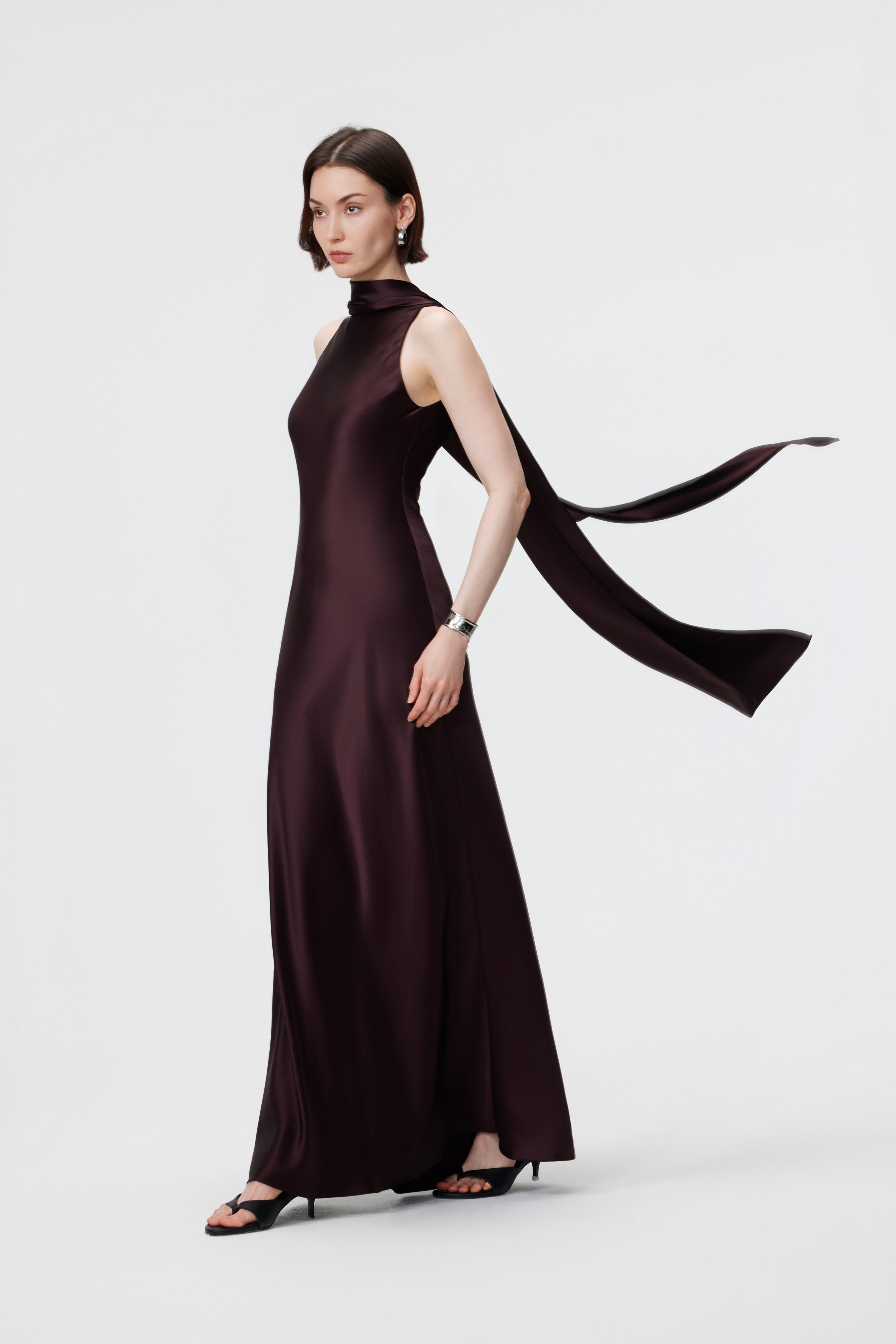 The AENSO Elara Gown in Espresso, styled in the signature high-neck profile; an architectural, statuesque look crafted from luminous Naia™ Acetate.