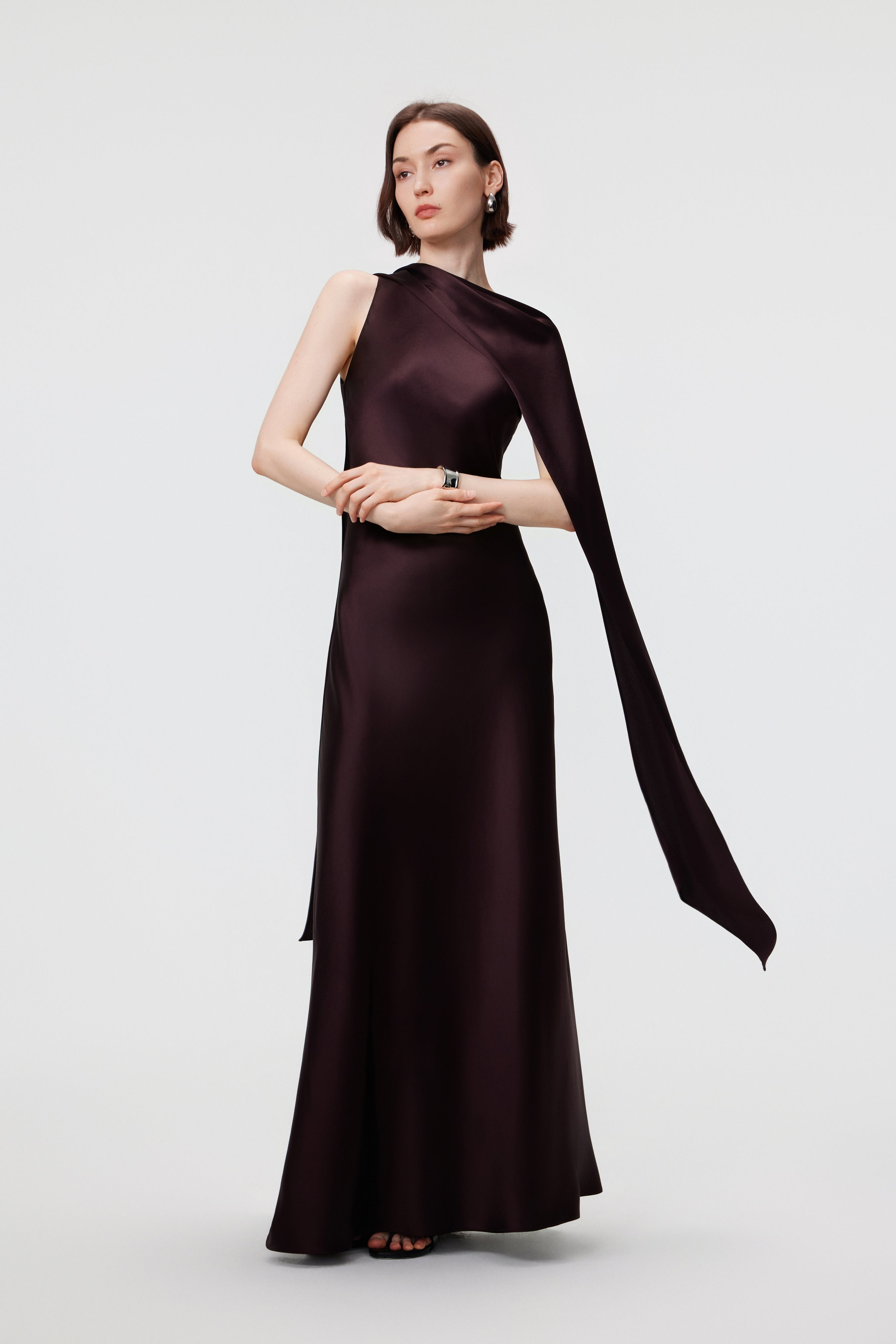 The AENSO Elara Gown in Espresso, styled in a one-shoulder silhouette, demonstrates the modular versatility of the integrated scarf for a modern, asymmetric look.