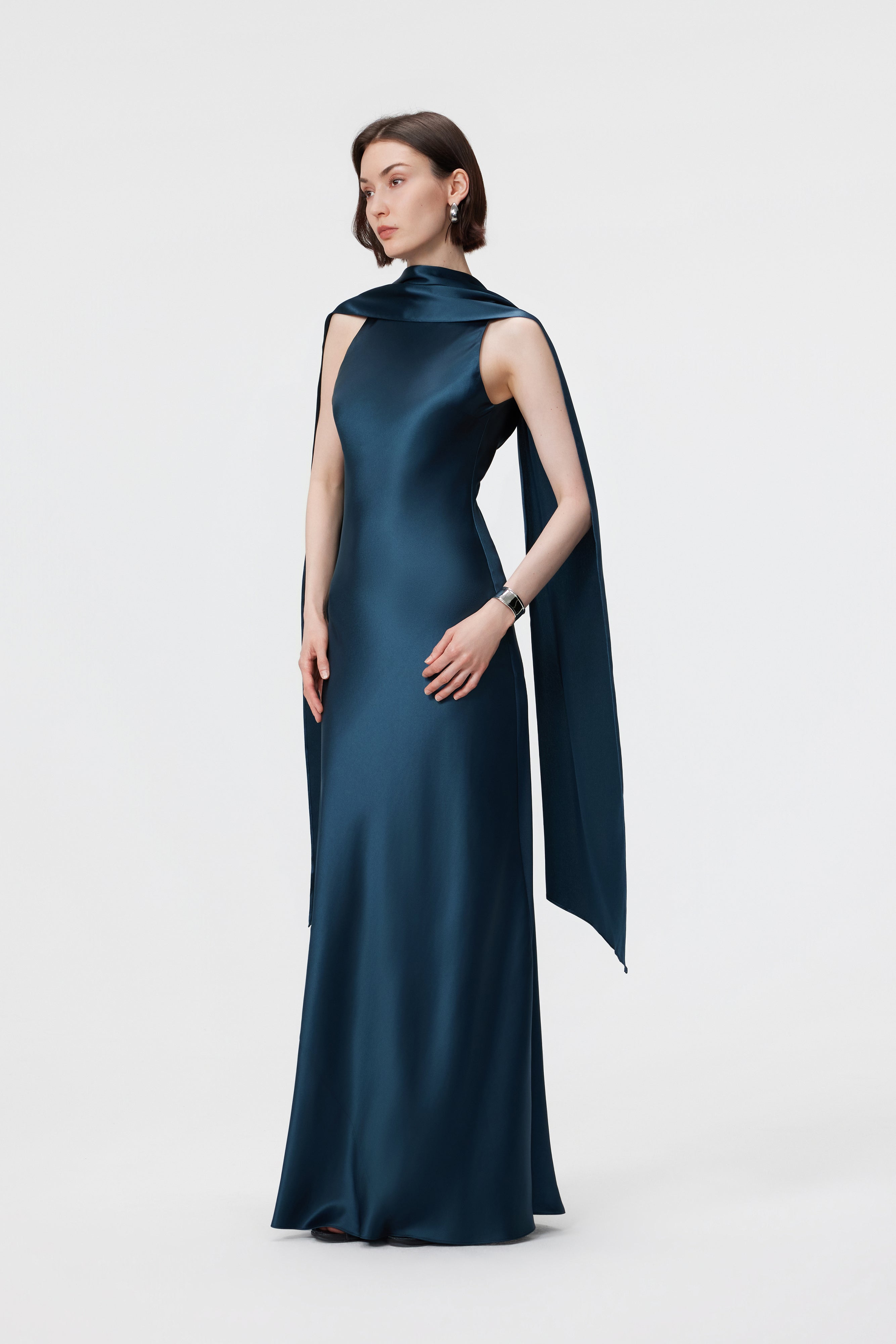 Side profile of the AENSO Elara gown in Midnight Teal; highlighting the dramatic, high-neck drape and the sleek, architectural line of the signature column silhouette in high-luster Naia™ acetate.