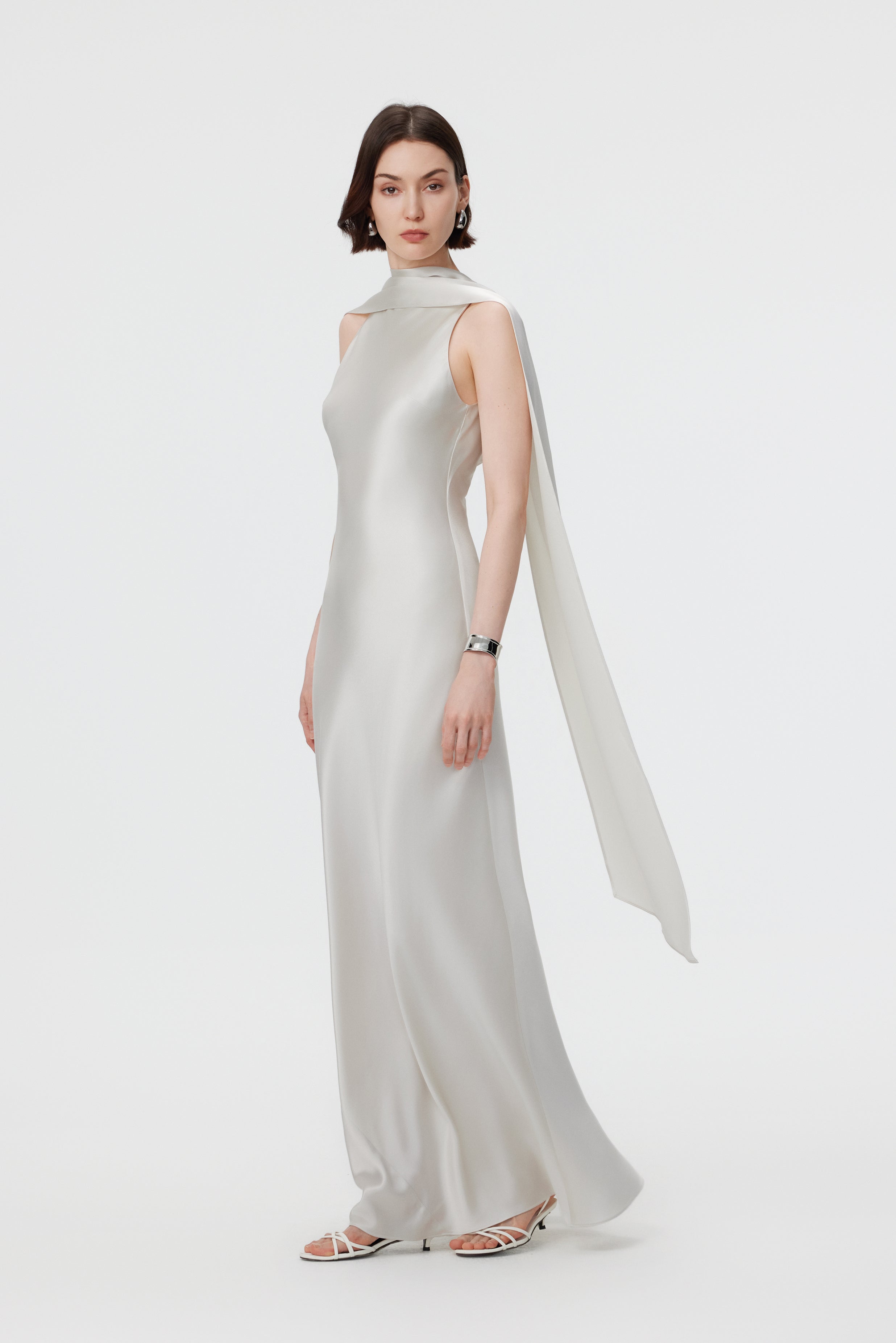 Side profile of the AENSO Elara gown in Pearl; showcasing the architectural drape of the integrated scarf and the sleek, statuesque lines of the bias-cut silhouette.
