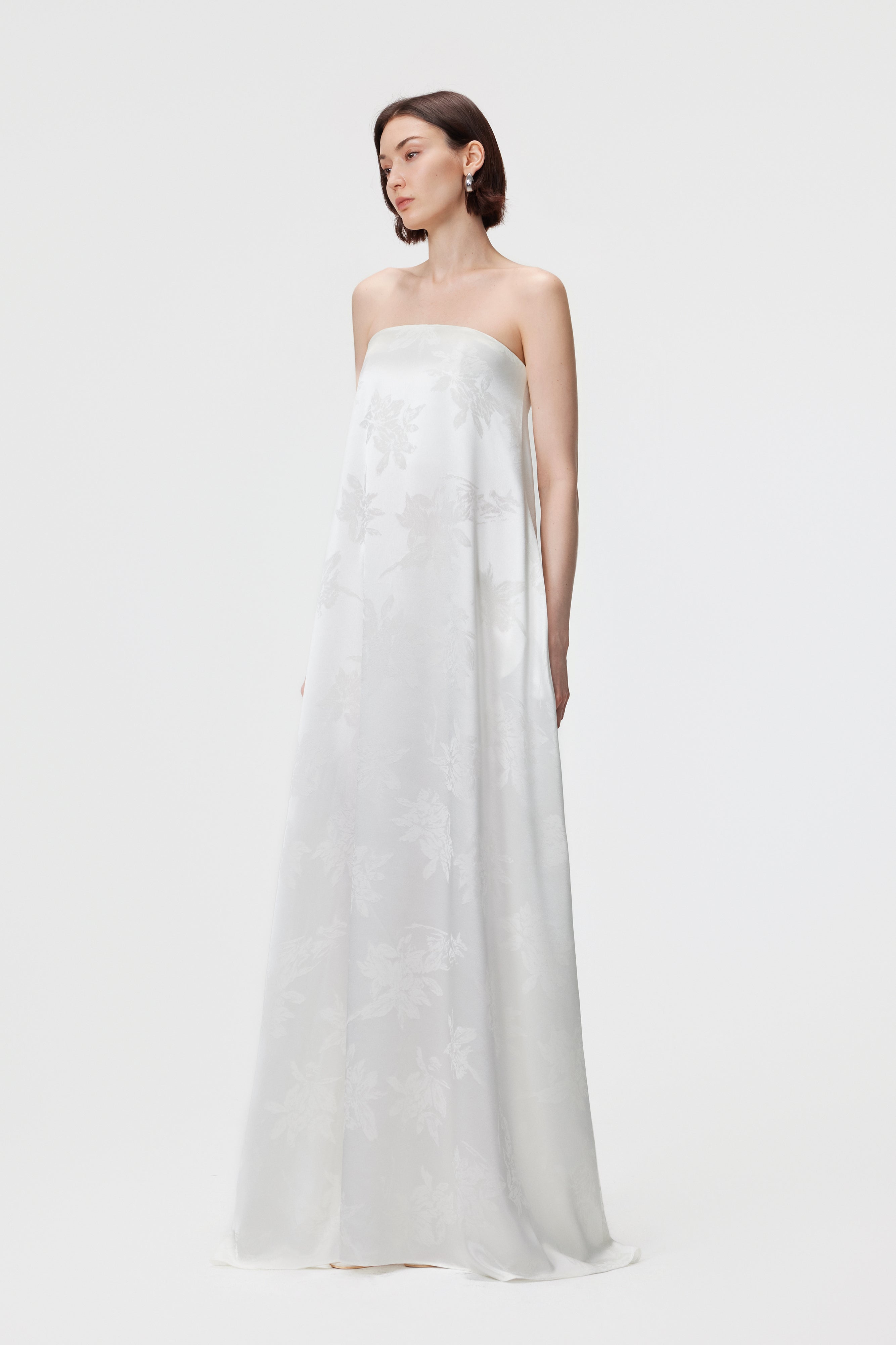 Side profile of the Iris Jacquard Bardot Maxi Dress in White, showcasing the straight-cut relaxed fit and the sculptural drape of the White floral jacquard. The shot emphasizes the clean vertical lines.