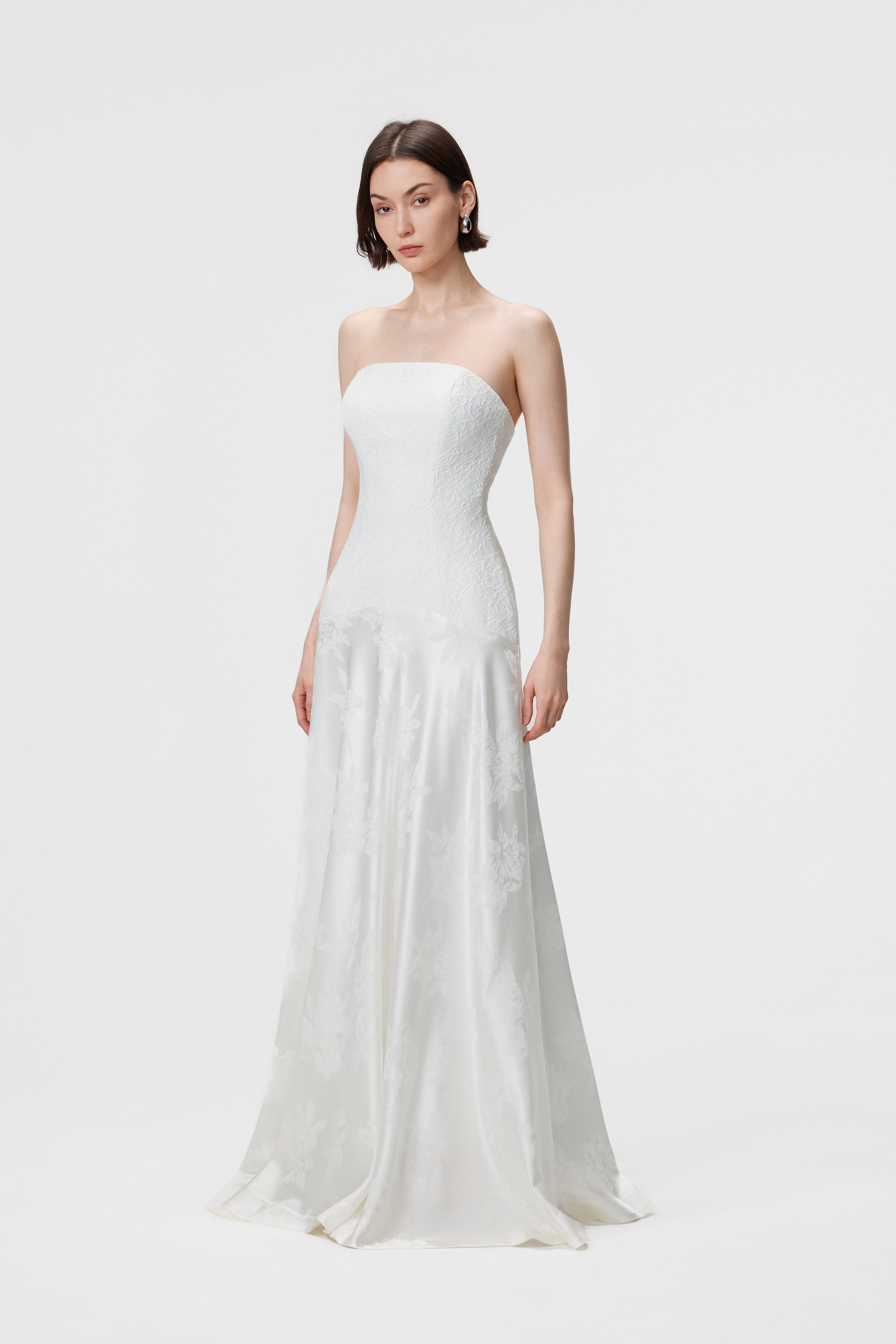 Aenso Vera Gown in Pearl white featuring a paneled lace bodice, sculptural curved neckline, and a bias-cut floral jacquard skirt for a grand, floor-length silhouette.