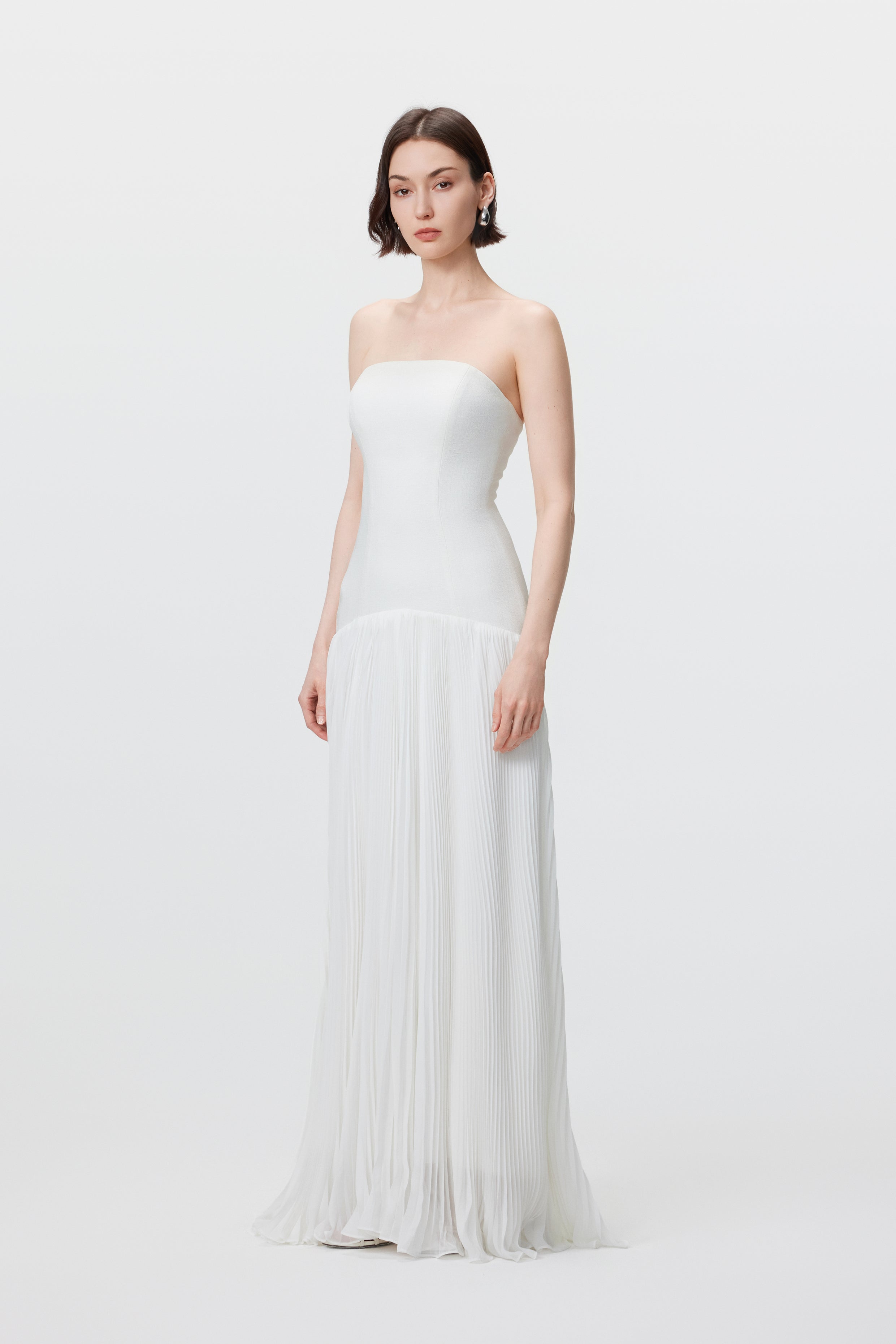 Side profile of the white Luna gown, showcasing the signature rhythmic architecture and the fluid transition from the high-waisted bodice to the floor-length pleated skirt.