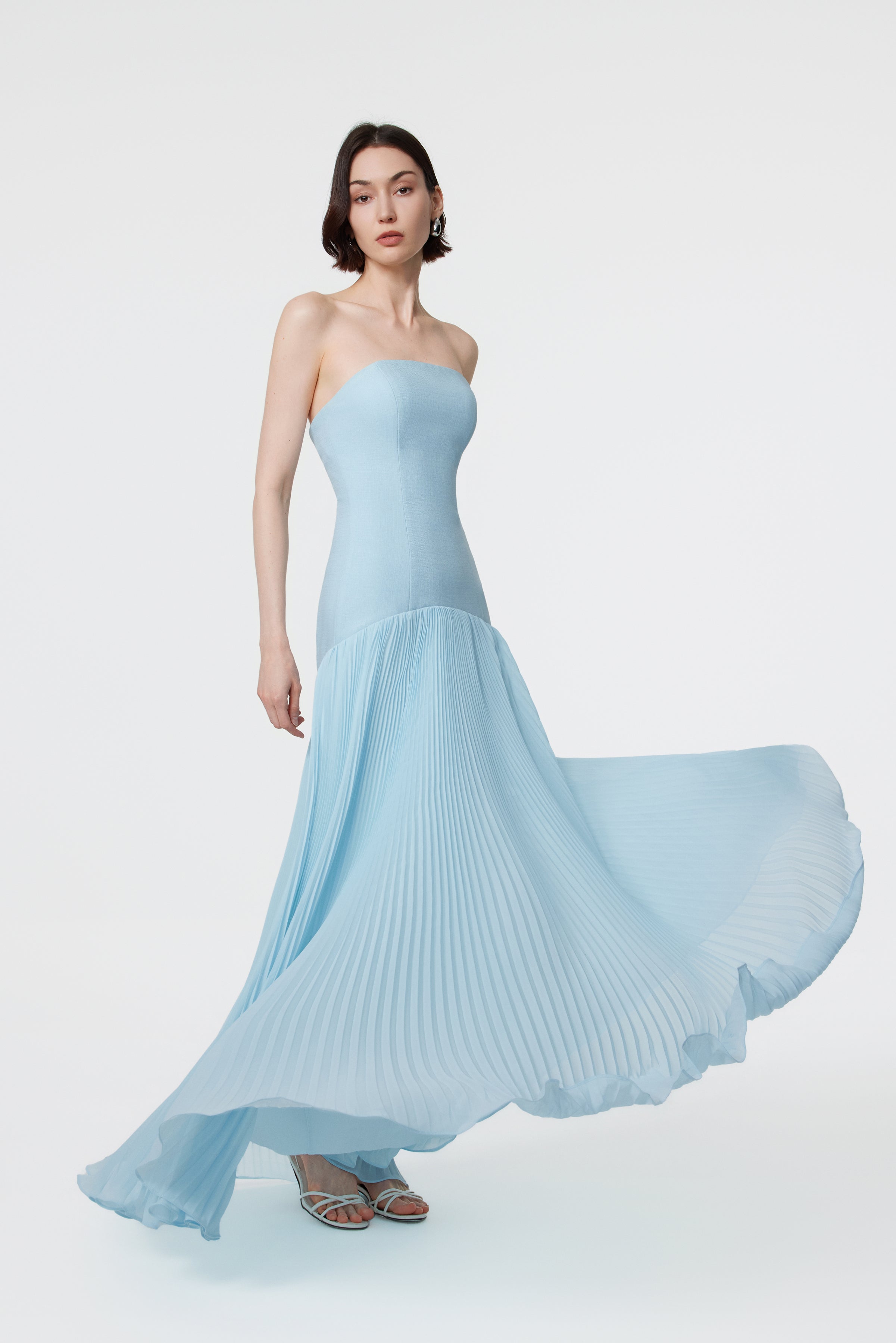 The Luna Gown in Ether Blue showing the weightless fluidity of the sunray pleated skirt and the elongated silhouette created by the signature dropped curved waist.