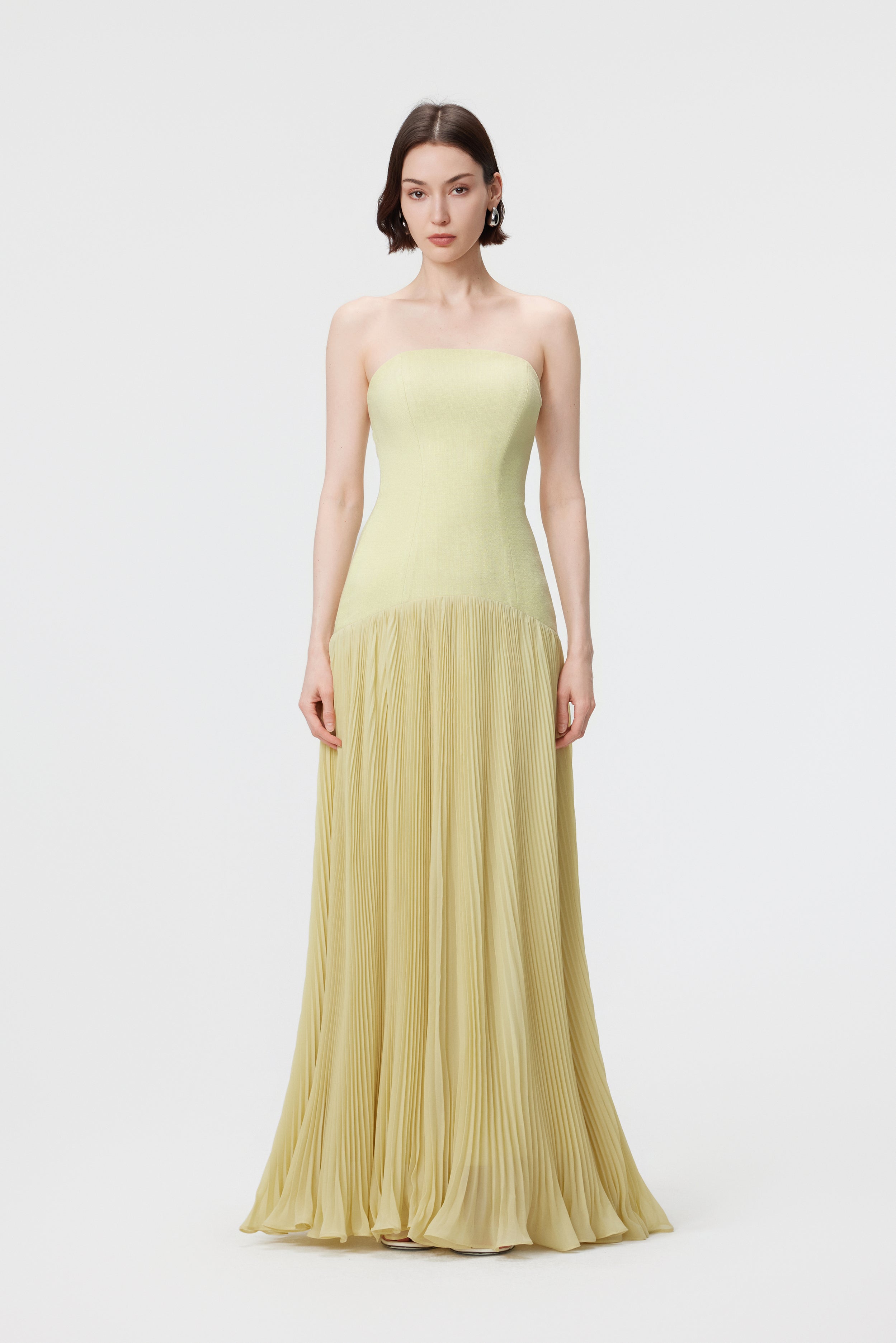 Static front view of the AENSO Luna gown in Citron; a pale, luminous yellow-green silhouette showcasing the precision-paneled bustier bodice and the crisp, vertical lines of the sunray pleats in sustainable slubbed Naia™ acetate.