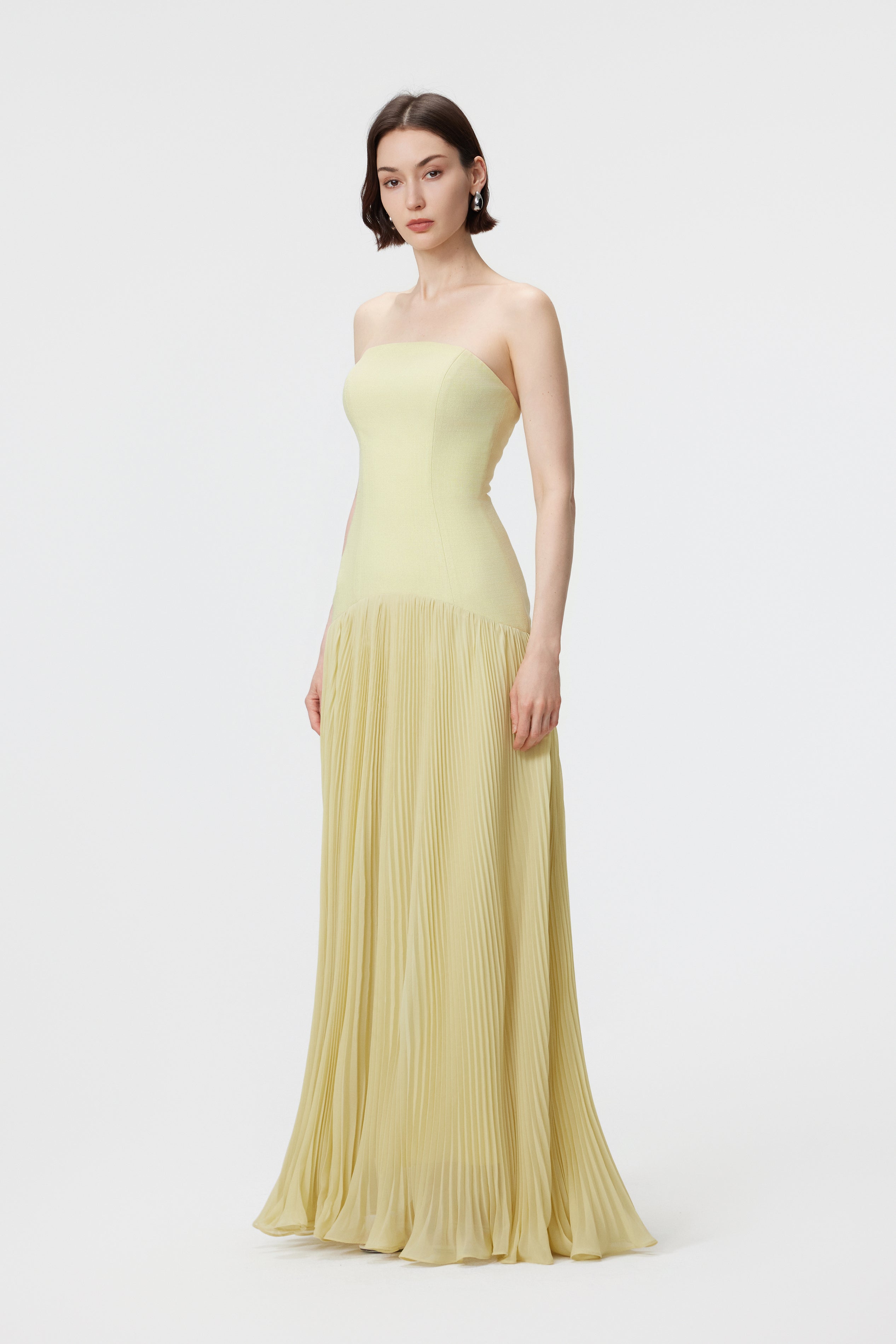 Side profile of the AENSO Luna gown in Citron; highlighting the structured bustier bodice and the elegant, floor-sweeping drape of the sunray pleats in sustainable slubbed Naia™ acetate.