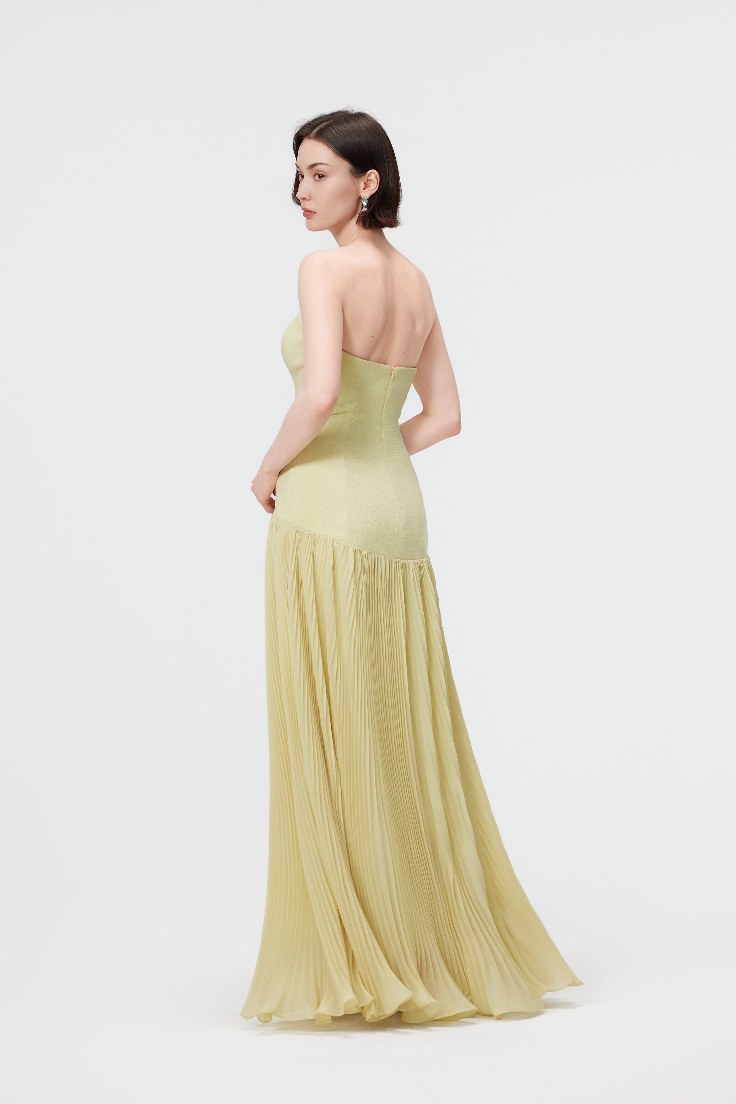 Back view of the AENSO Luna gown in Citron; showcasing the clean, minimalist lines and the continuous flow of the architectural pleats from the waist to the floor-length hem.
