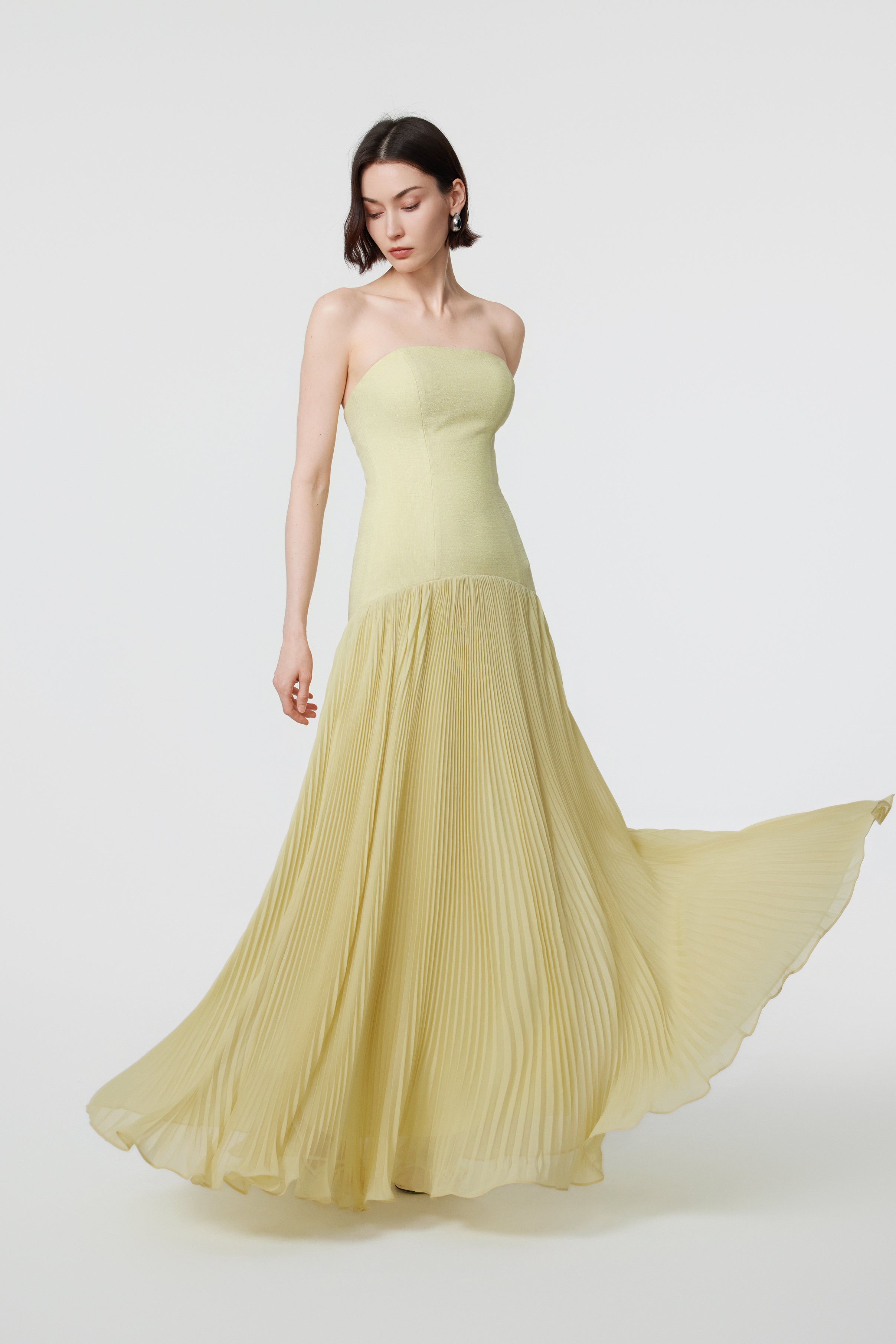 The AENSO Luna gown in Citron in motion; the voluminous floor-length pleats flare dramatically, capturing the fluid serenity and soft, crystalline luster of the yellow-green fabric.