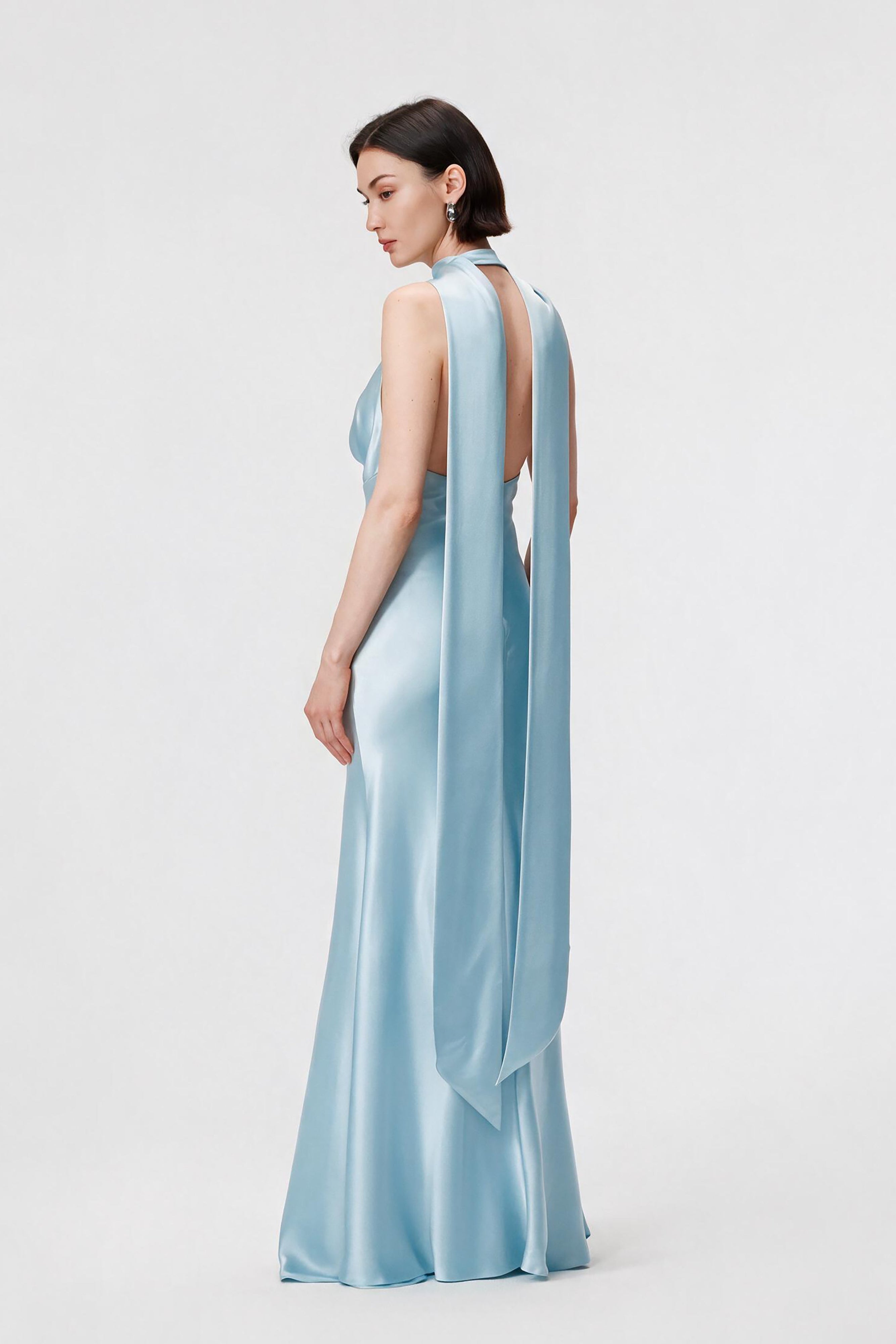 Model from the back wearing the Rhea dress in Ether Blue, highlighting the fluid cowl neckline, low open back, and floor-length, bias-cut silhouette in luminous Naia™ Acetate satin.