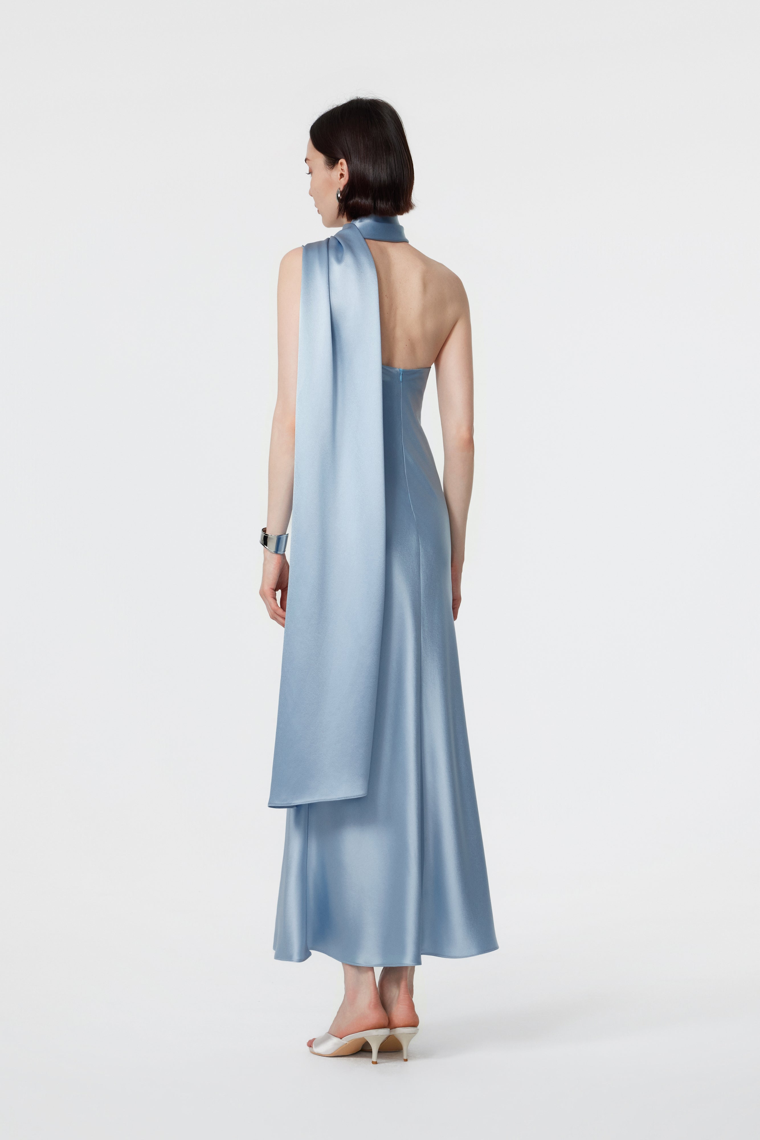 Rear view of the Lyra dress in Glacial Mist, showcasing the bare-back silhouette and the trailing finish of the high-neck wrap.