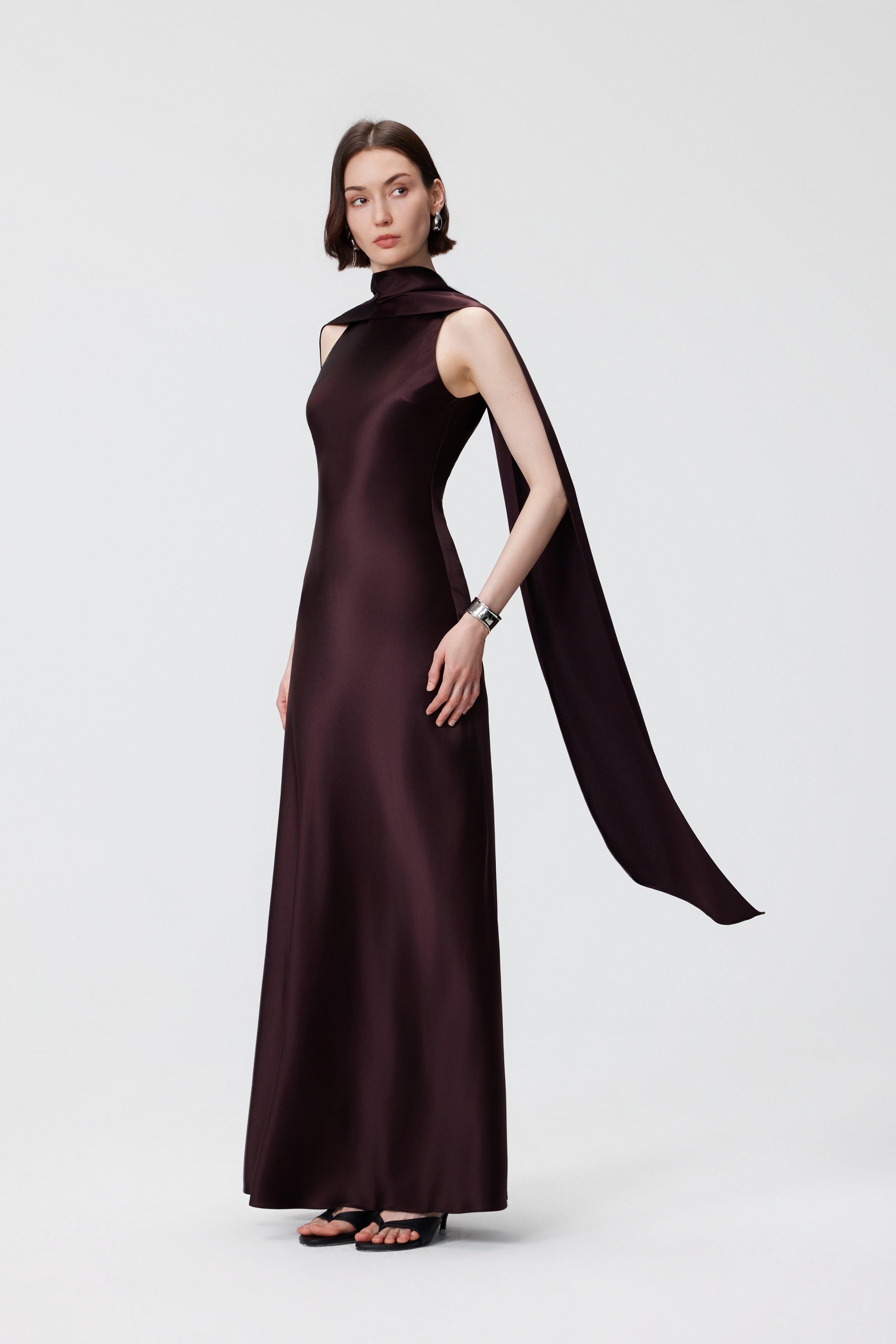 Side profile of the AENSO Elara Gown in Espresso, showcasing the sculptural depth and the rhythmic, liquid-like drape of the bias-cut silhouette.