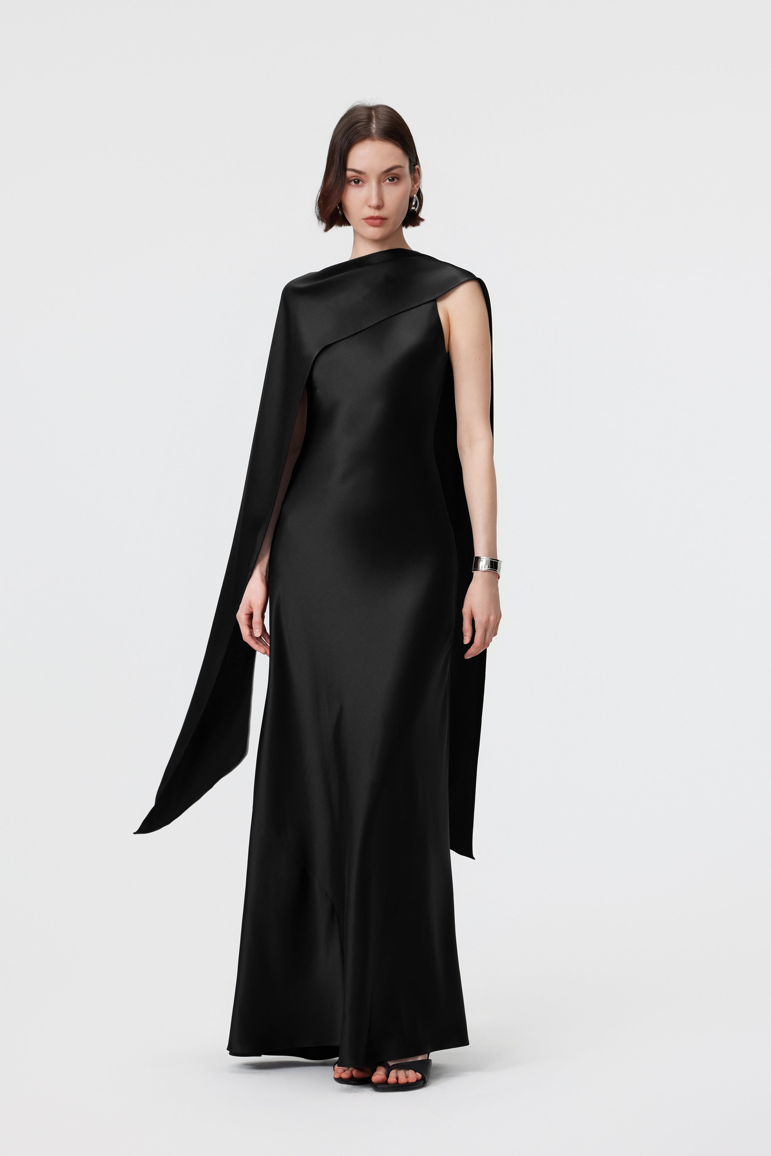 AENSO Elara Gown in Black, styled as an asymmetric cape to demonstrate the multi-way integrated scarf in liquid-like satin.