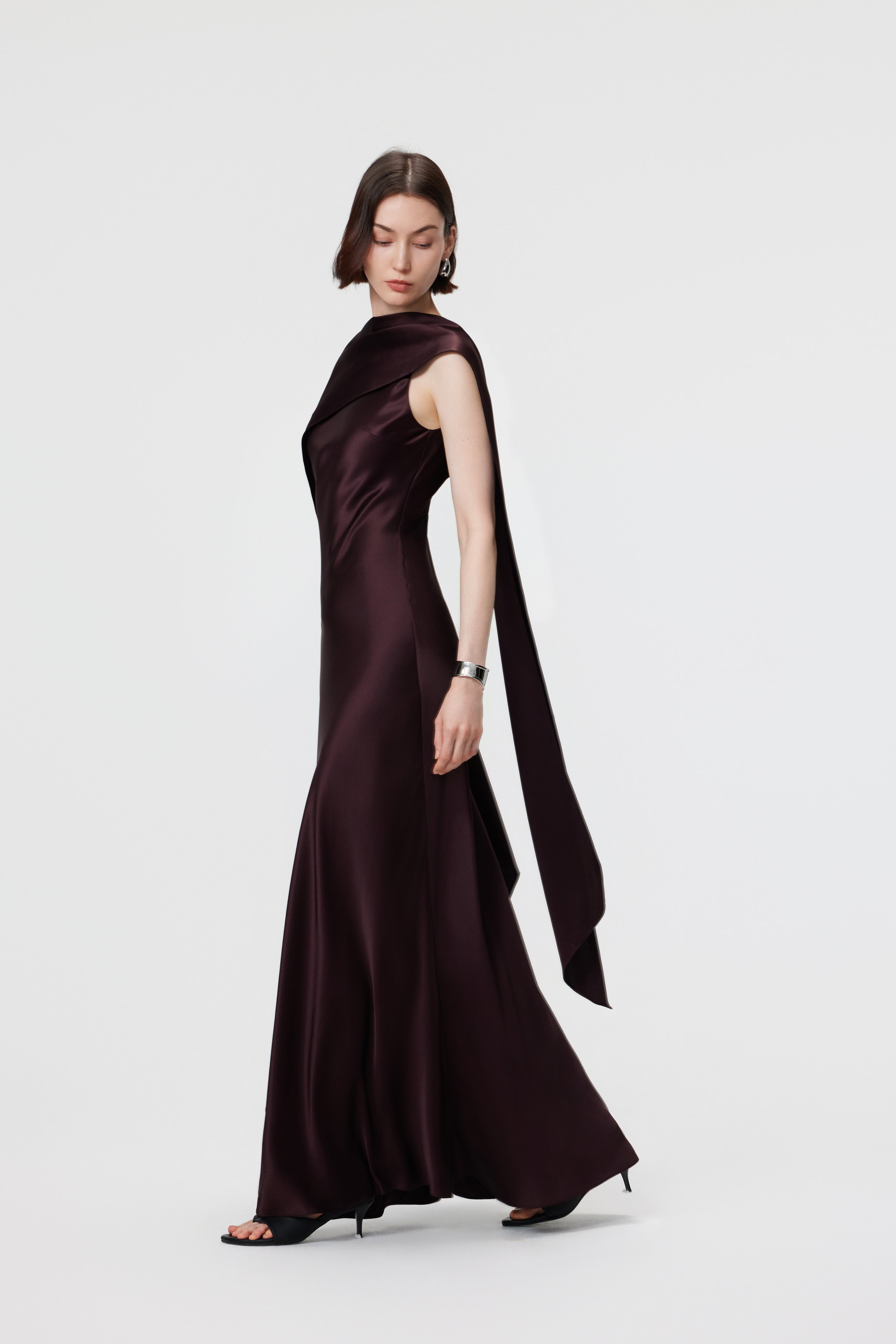 The AENSO Elara Gown in Espresso, styled in an asymmetric cape configuration, showcases the liquid-like movement and architectural edge of luminous Naia™ Acetate.