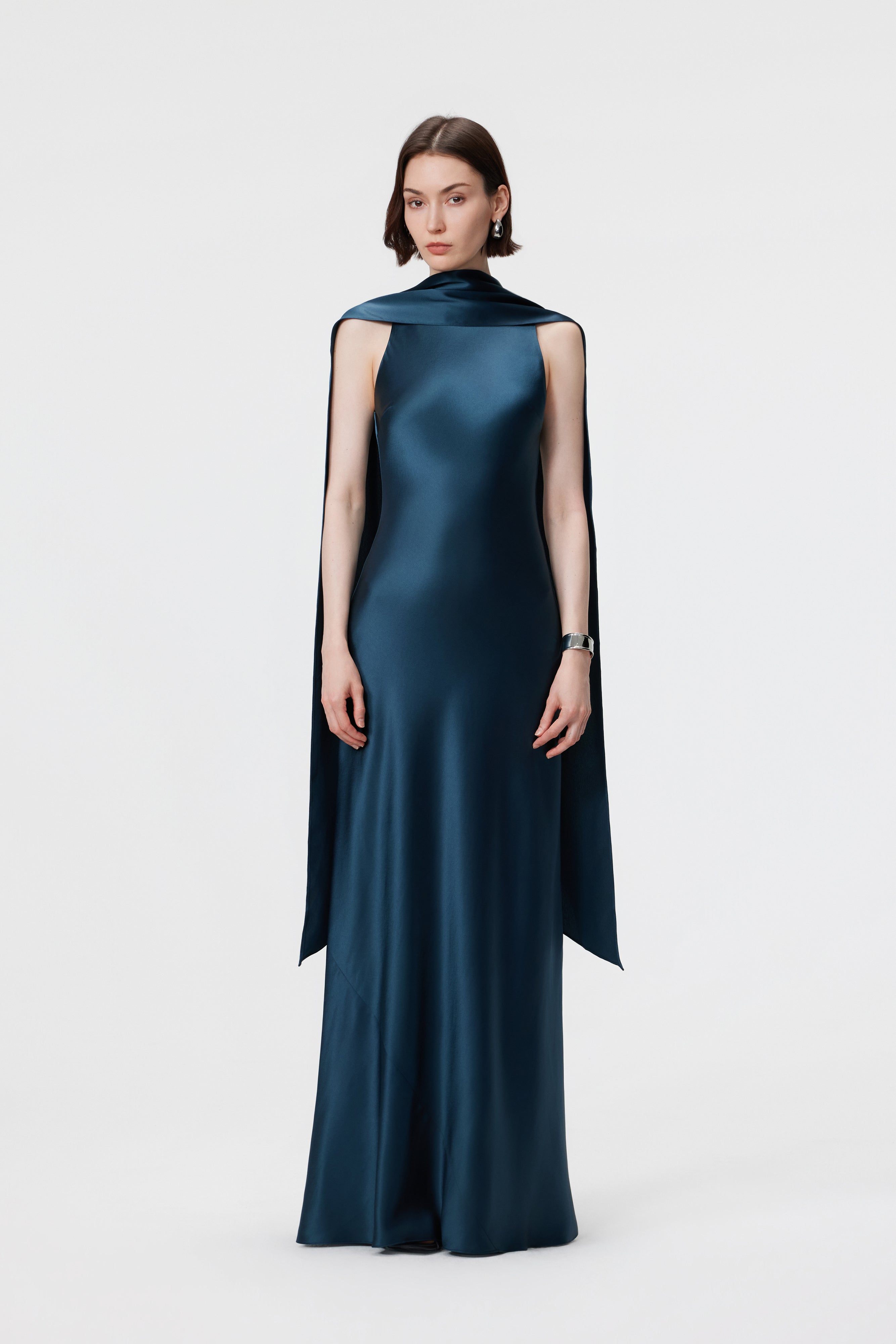 Static front view of the AENSO Elara gown in Midnight Teal; a signature column silhouette featuring a dramatic, convertible high-neck drape in high-luster Naia™ acetate.