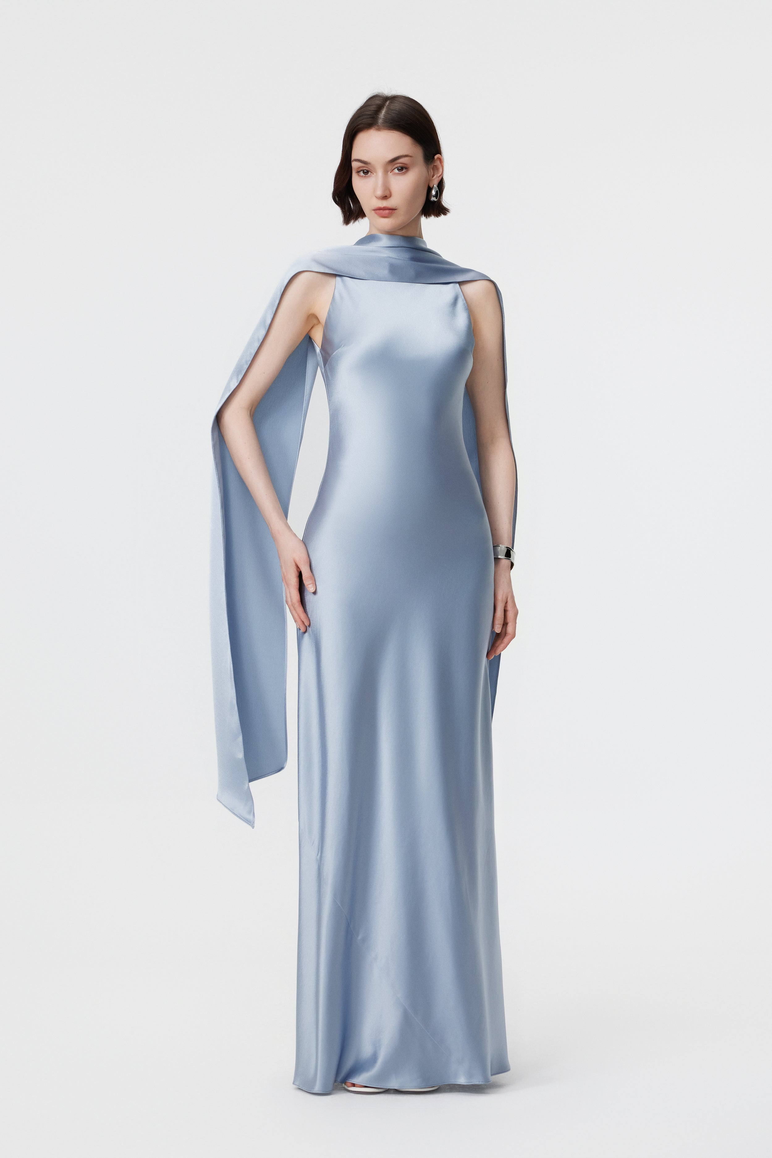 Full-length front view of the AENSO Elara gown in Dove Blue; the high-luster Naia™ Acetate catches the light to reveal the rhythmic, liquid-like trail of the bias-cut skirt and the statuesque grace of the high-volume silhouette.