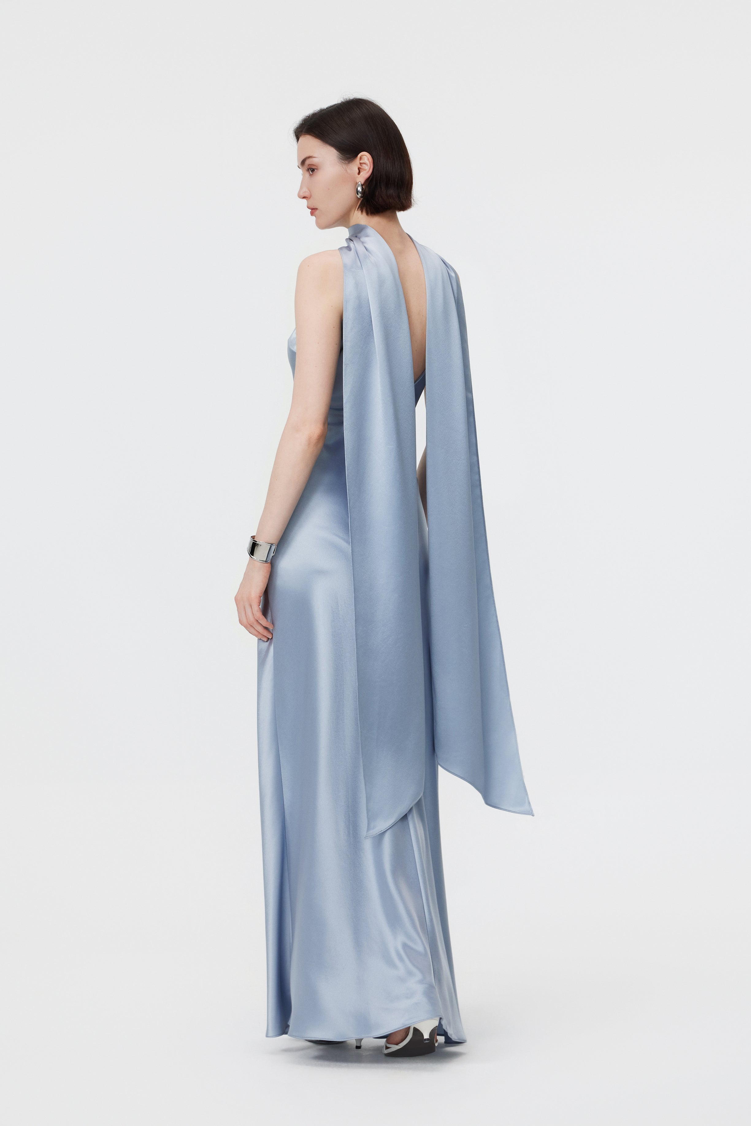 Back view of the AENSO Elara gown in Dove Blue; showcasing the seamless, statuesque line of the bias-cut construction and the fluid, rhythmic trail of the high-luster Naia™ Acetate.