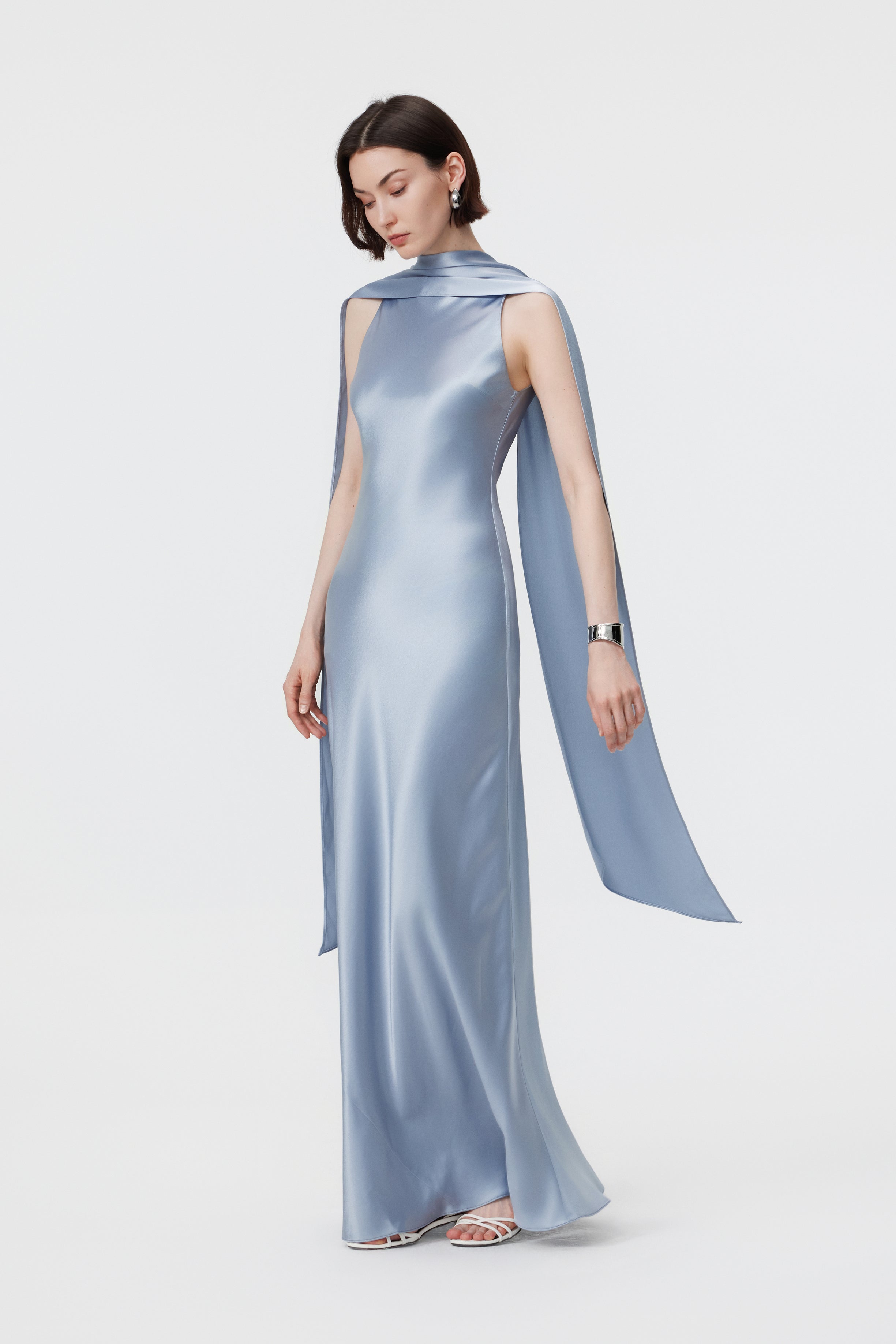 Side profile of the AENSO Elara gown in Dove Blue in motion; the bias-cut construction creates a rhythmic, liquid-like trail that highlights the cool-toned luster and sculptural depth of the fabric.