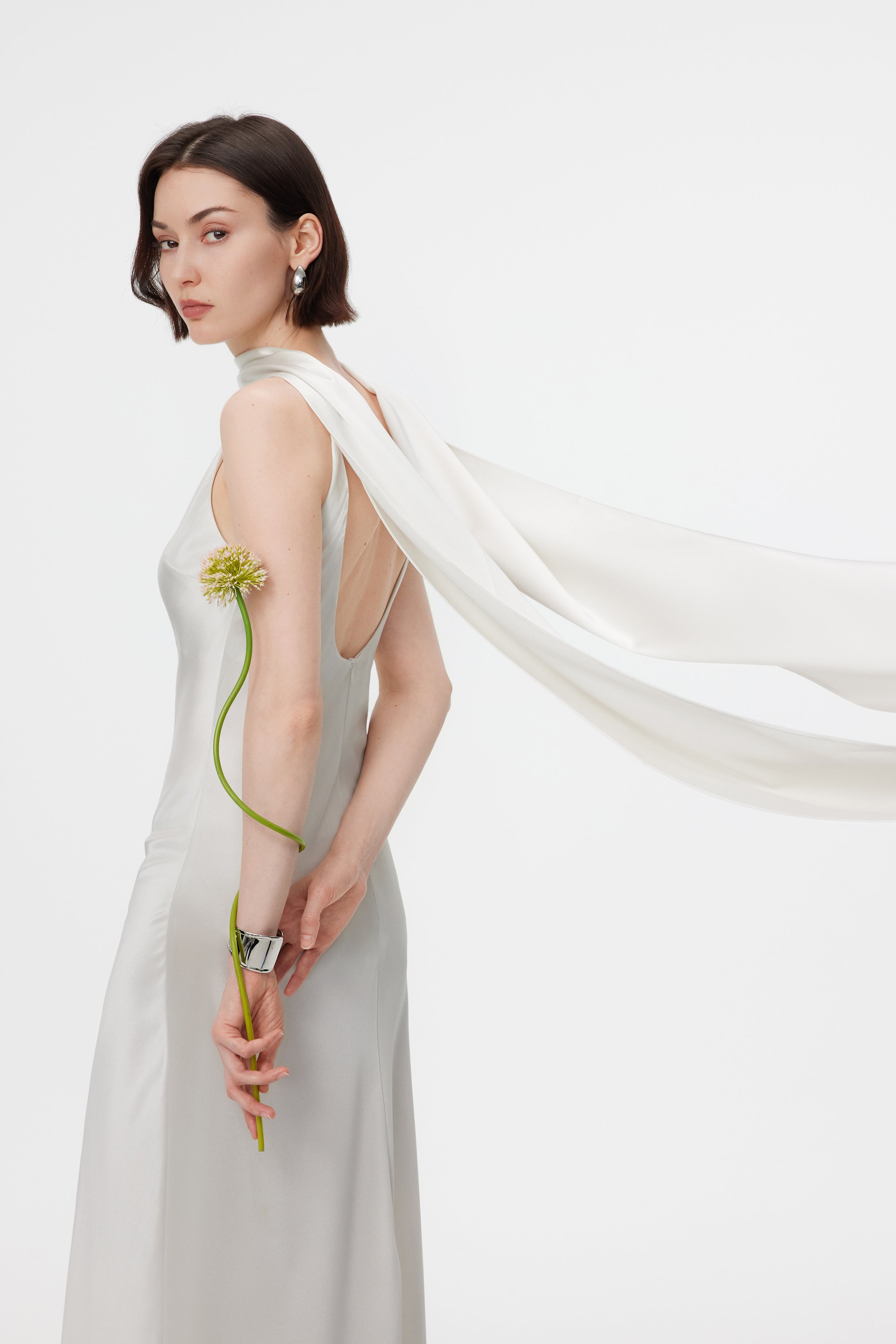 Close-up view of the AENSO Elara gown in Pearl in motion; capturing the rhythmic, liquid-like ripples of the lustrous Naia™ Acetate as the integrated scarf drapes into sculptural, high-saturation shadows.