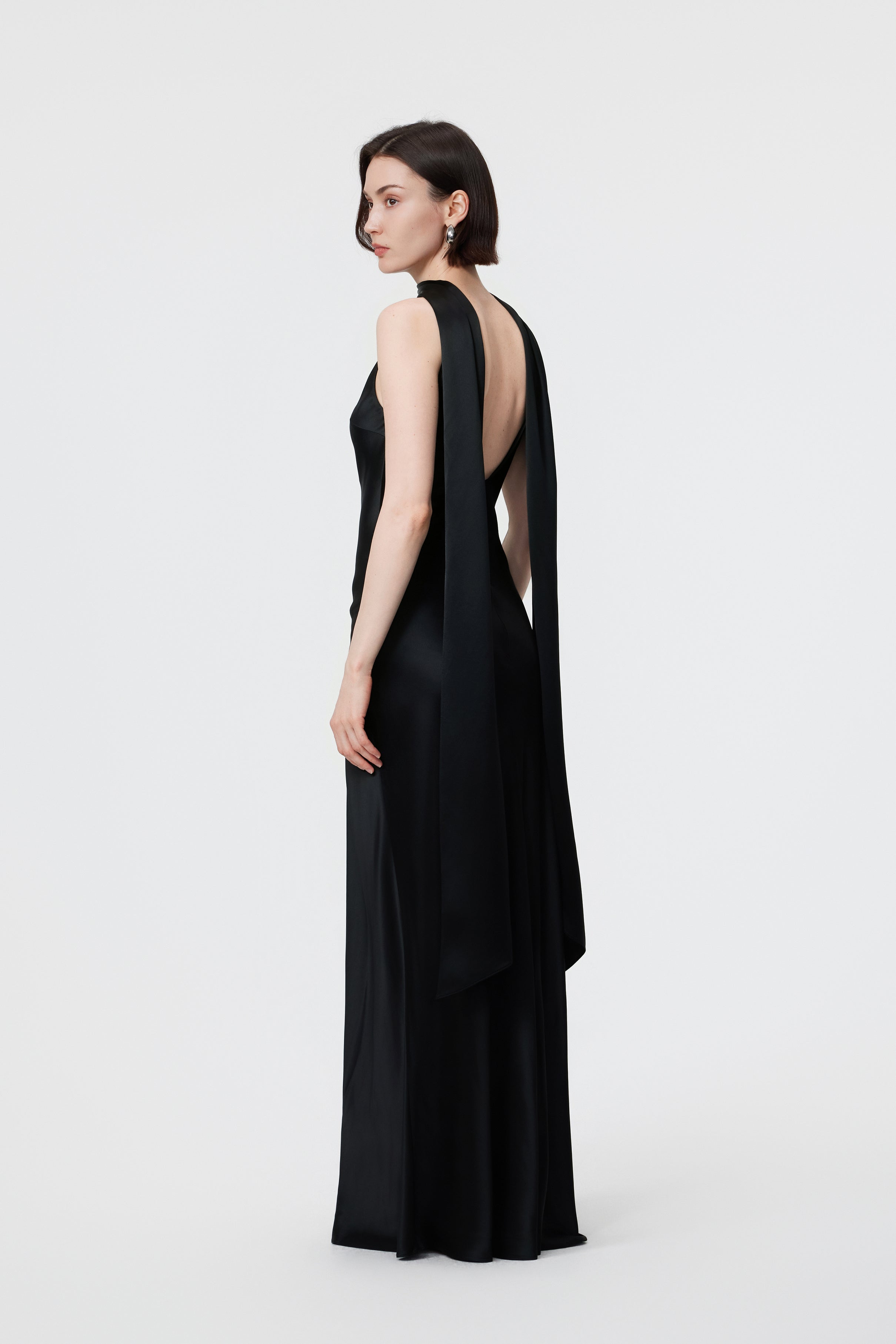Back view of the AENSO Elara gown in Black; emphasizing the fluid, rhythmic trail of the high-luster Naia™ Acetate and the clean, minimal construction.