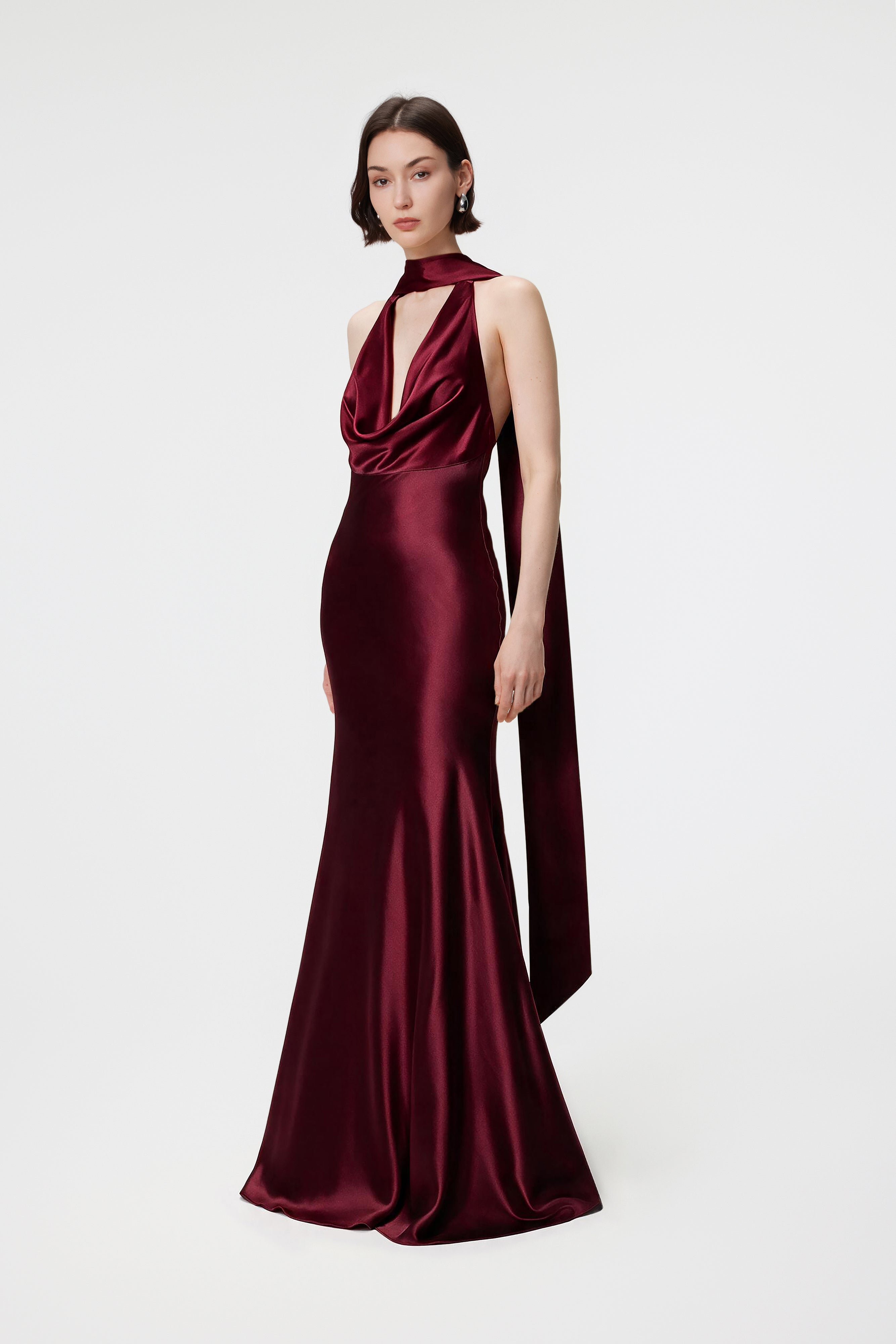 Model from the side wearing the Rhea dress in Red Berry, highlighting the fluid cowl neckline, low open back, and floor-length, bias-cut silhouette in luminous Naia™ Acetate satin.
